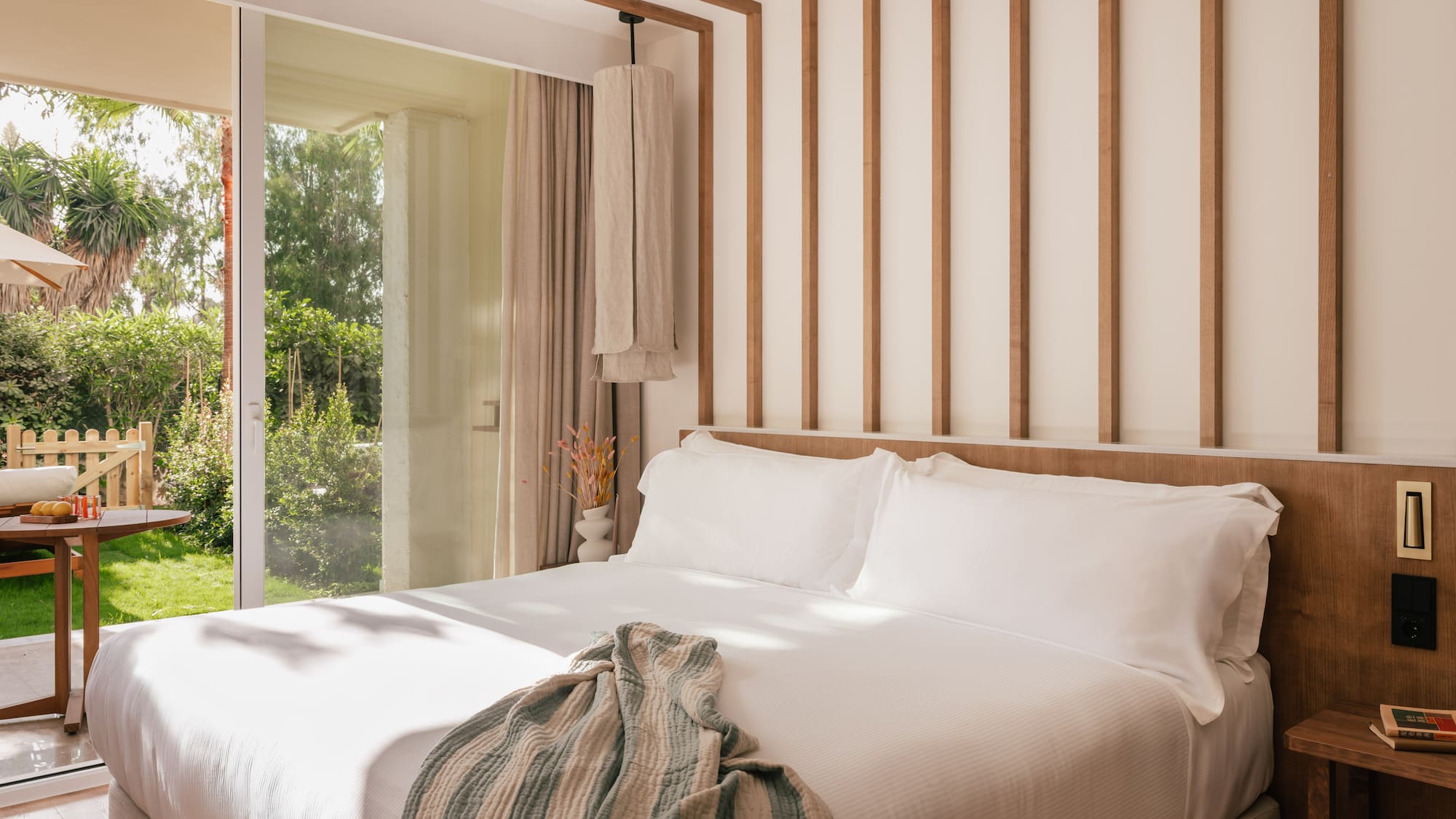 a bed with white sheets and pillows in a room with glass doors