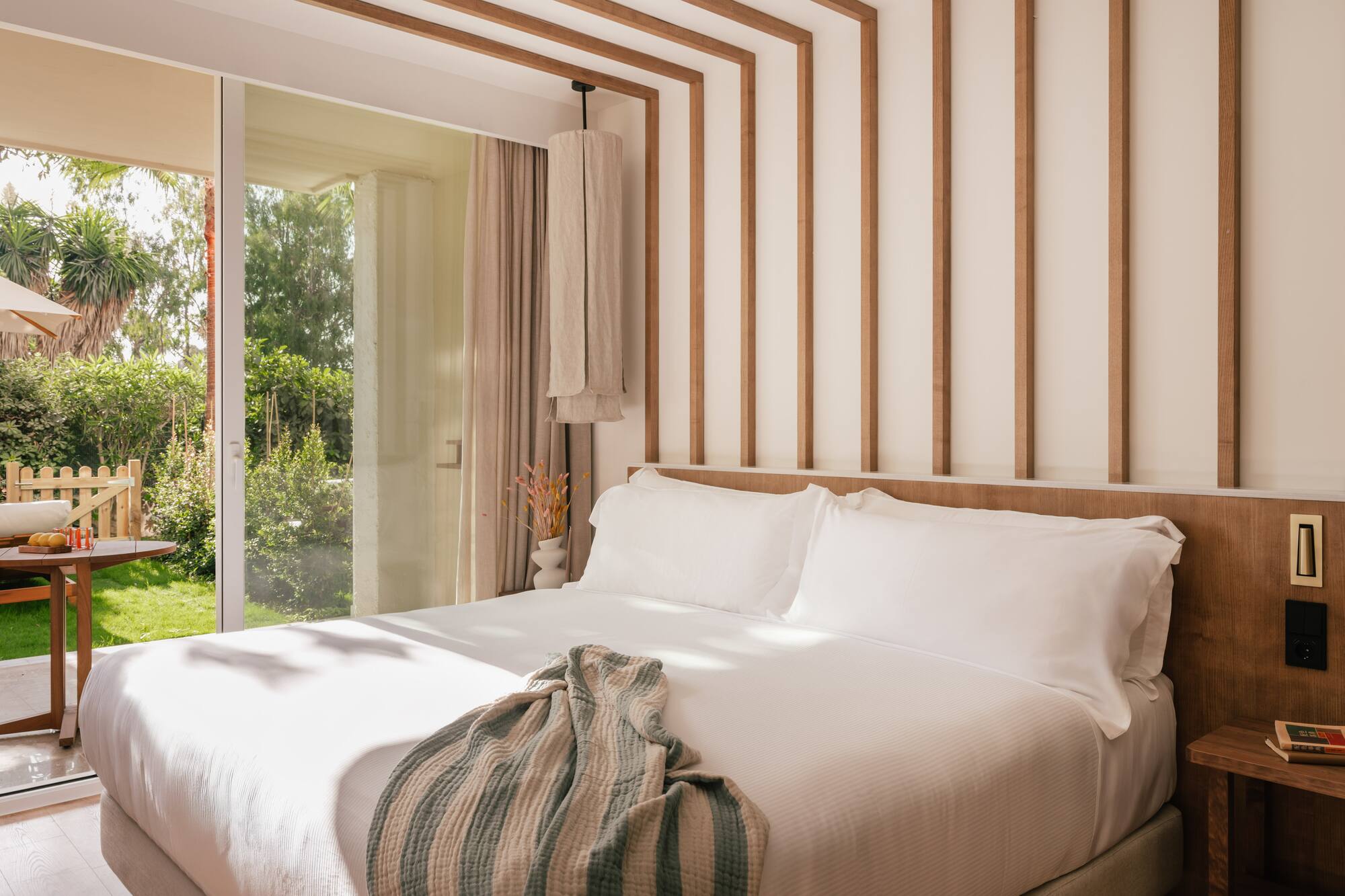 a bed with white sheets and pillows in a room with glass doors