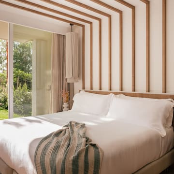 a bed with white sheets and pillows in a room with glass doors