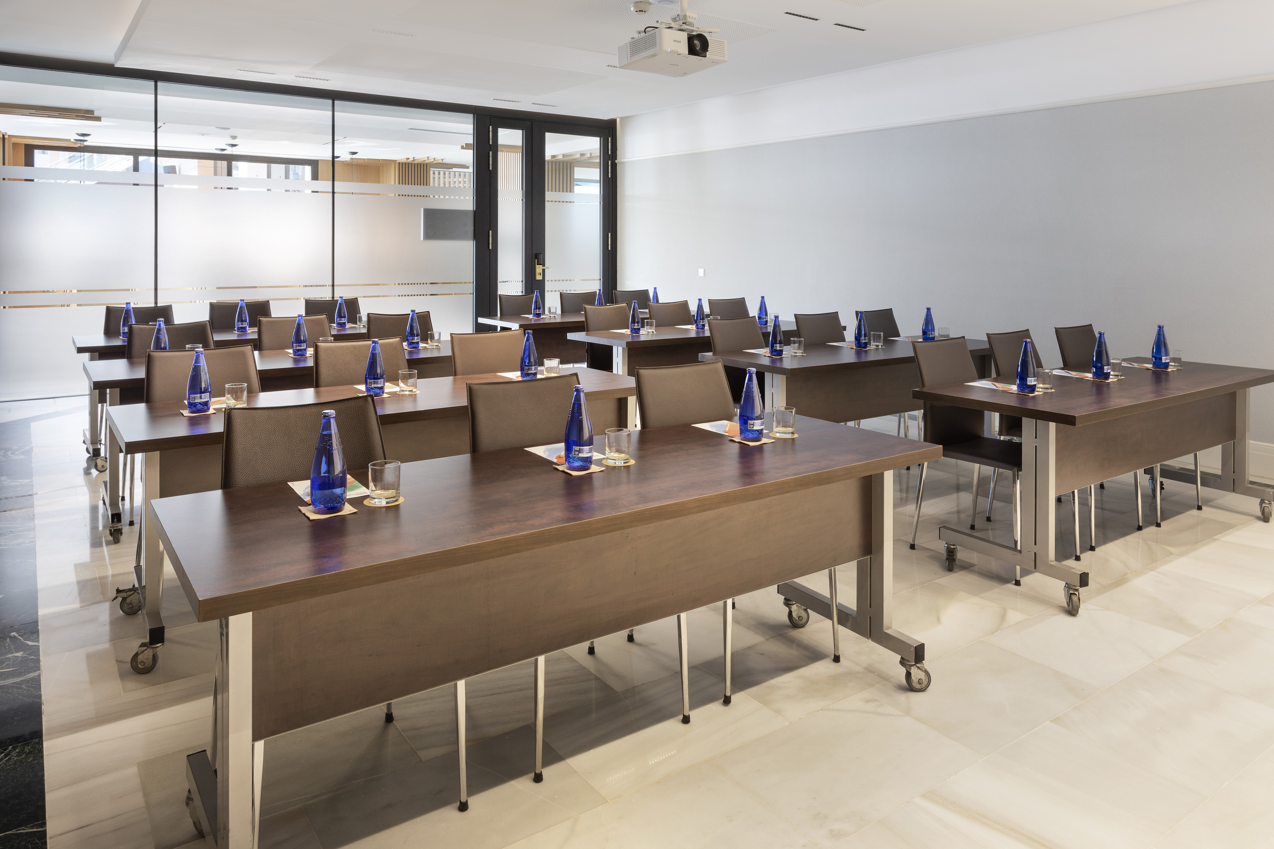 Modern conference room with tables, chairs, water bottles, and ceiling projector.