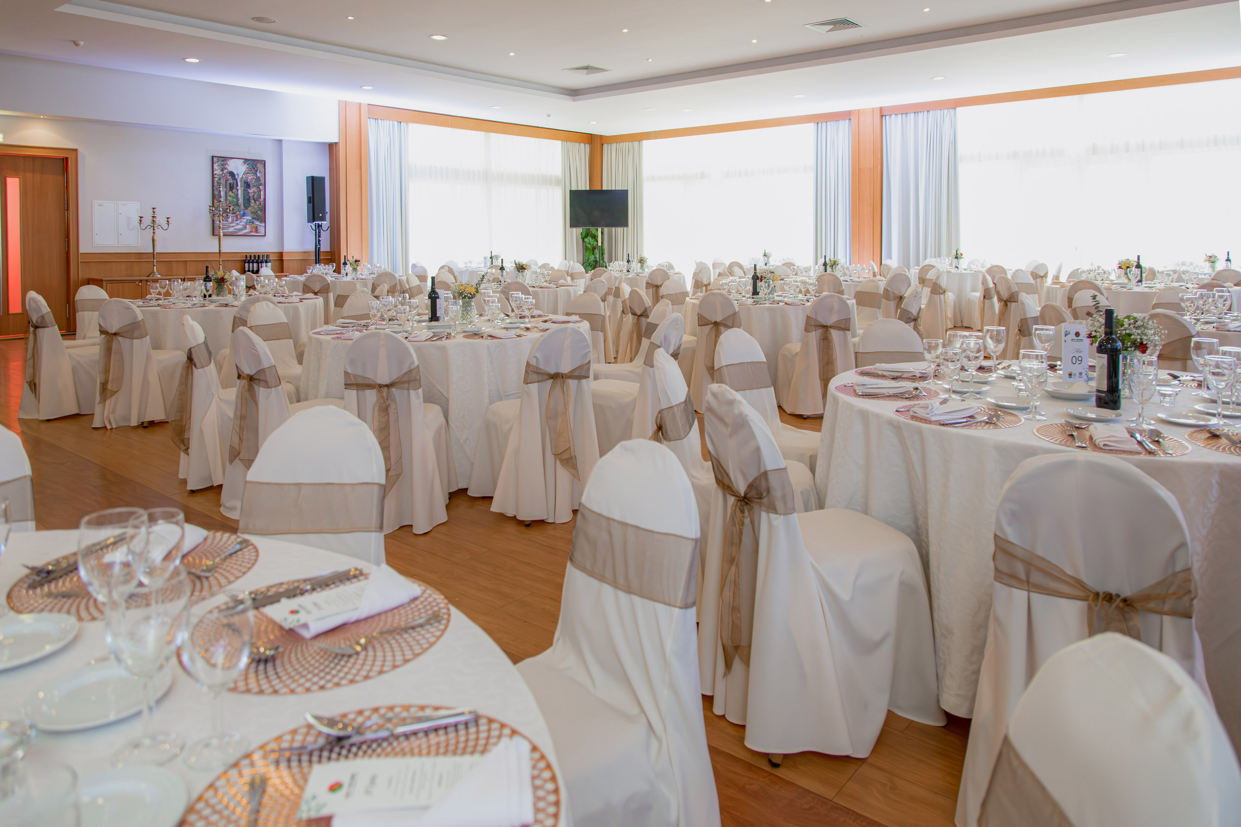 Elegant event hall with white tables and chairs, brown sashes, ready for banquet.