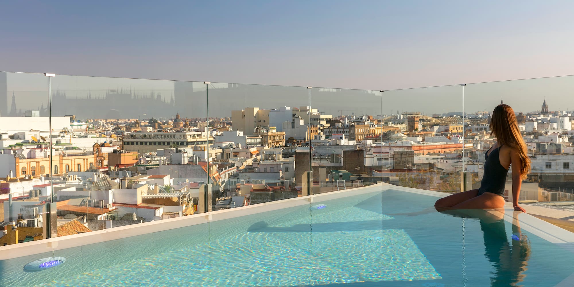 Mujer en piscina infinita de azotea, vistas panorámicas a Sevilla.