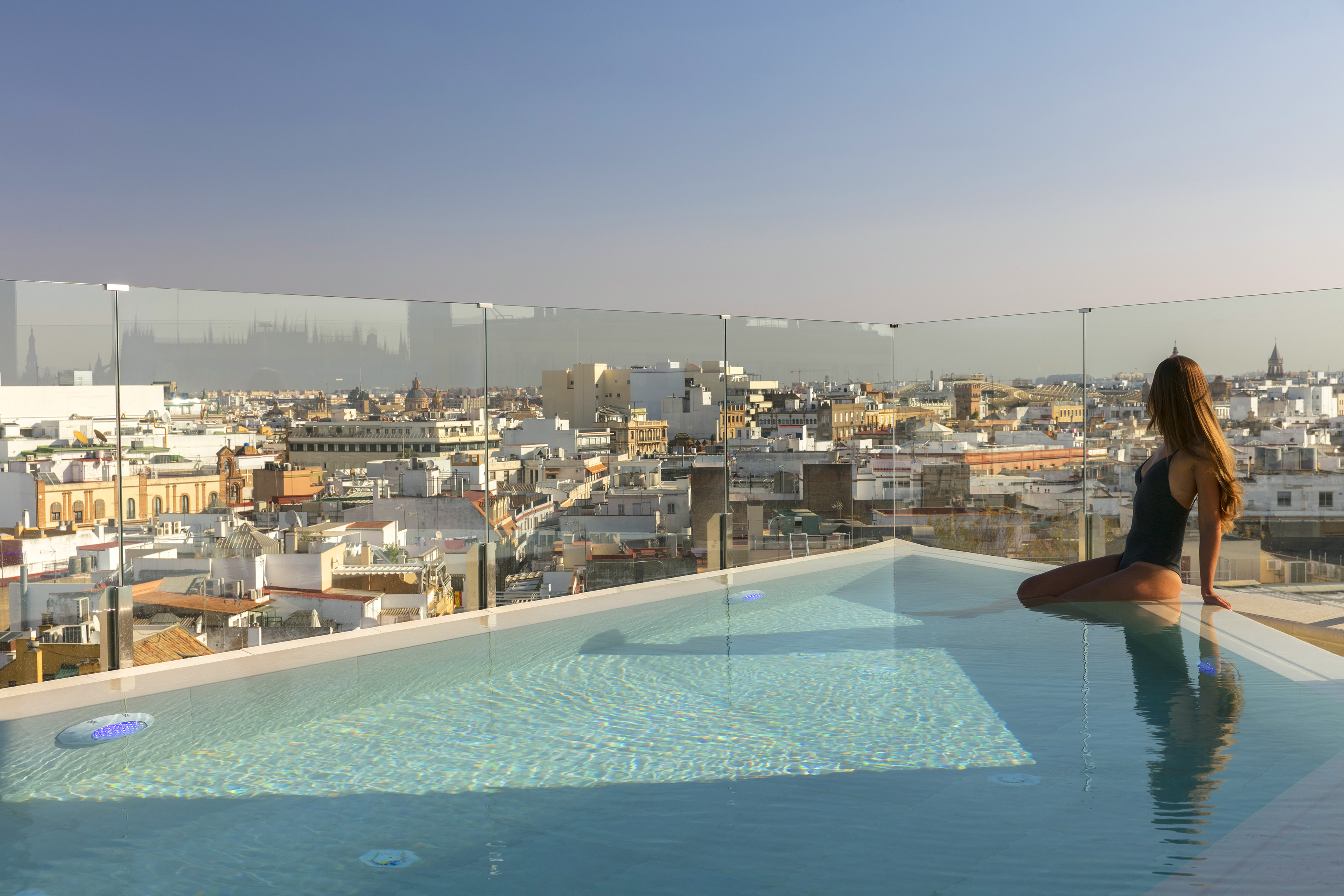 Mujer en piscina infinita de azotea, vistas panorámicas a Sevilla.