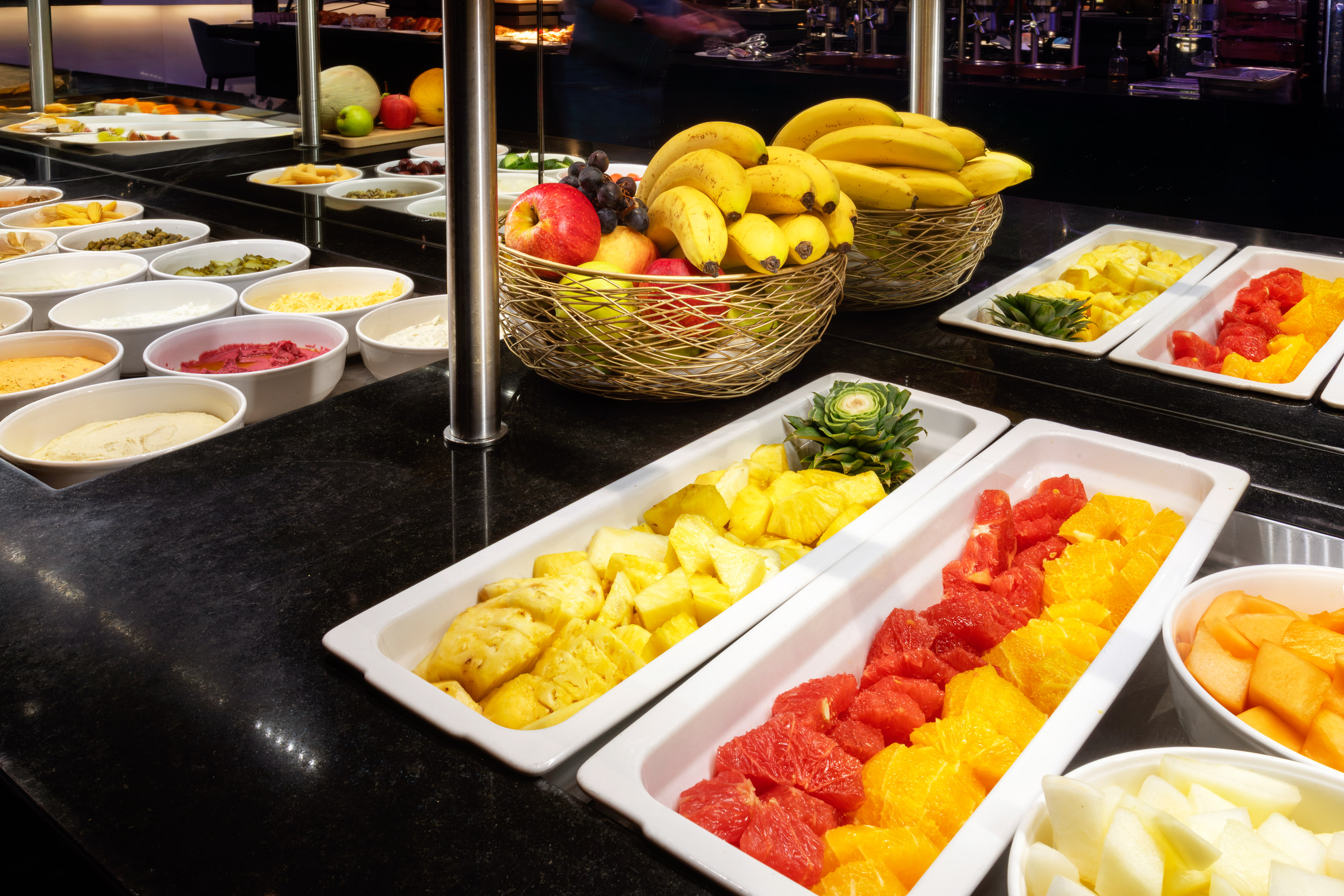 Fresh fruit buffet with bananas, pineapple, citrus, and healthy salad bowls.