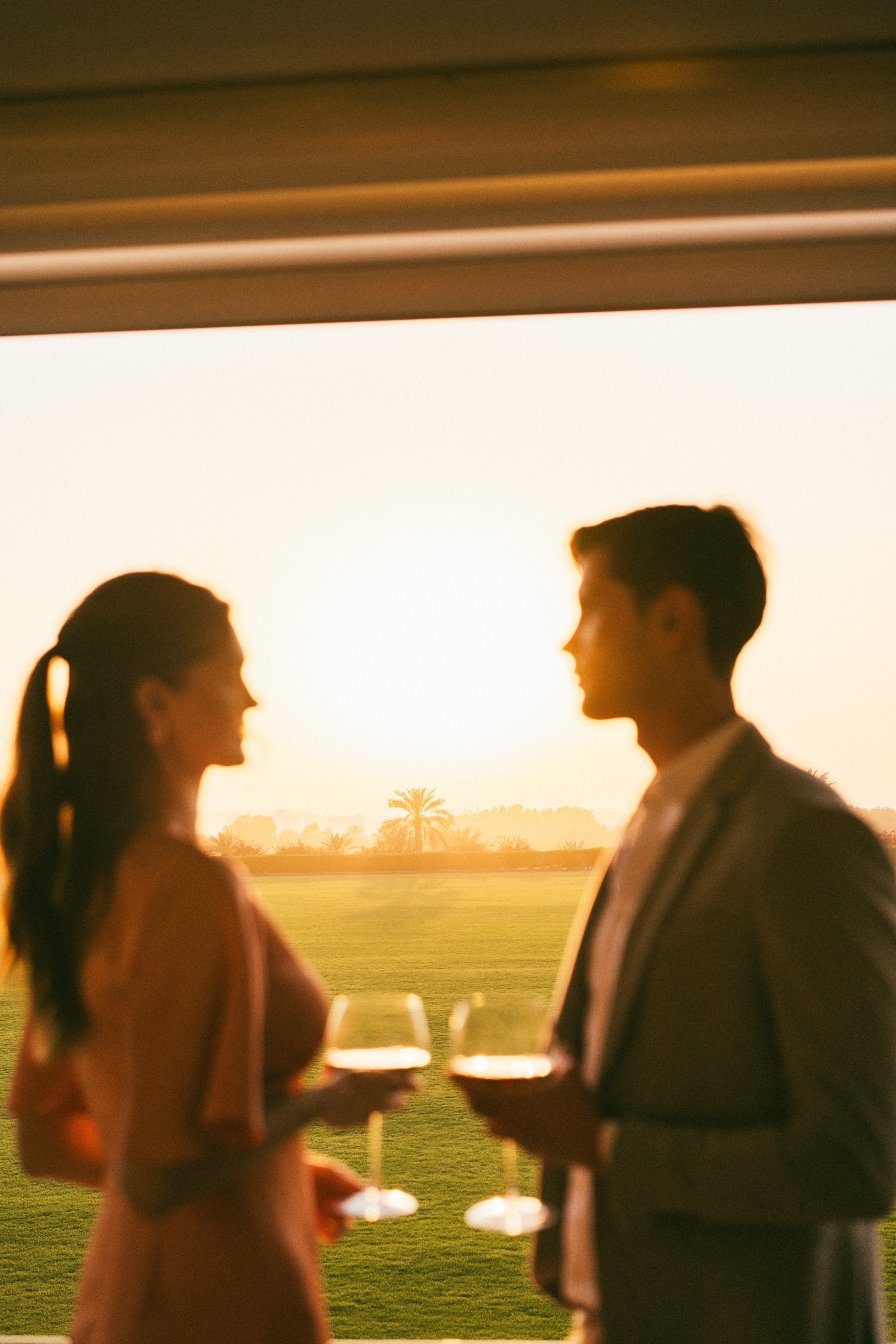Silhouetted couple enjoying wine at golden hour over a lush golf course.
