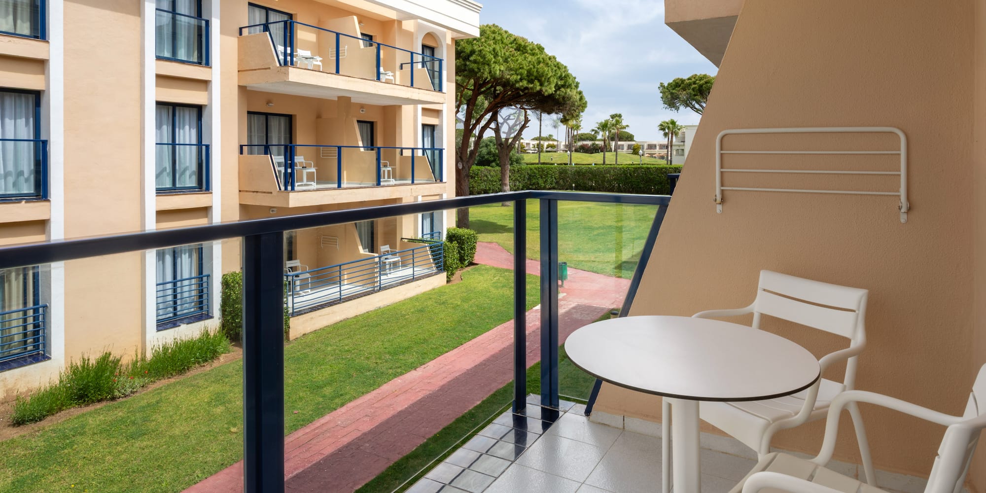 Resort balcony with white outdoor furniture and a lush green garden view.
