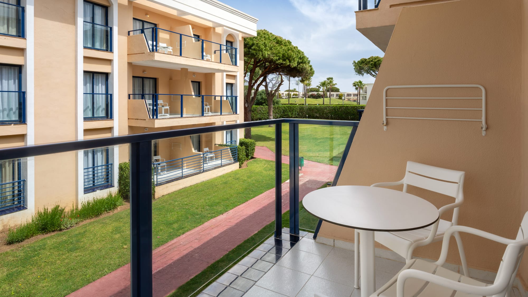 Hotel balcony with outdoor seating, view of resort buildings, and green garden.