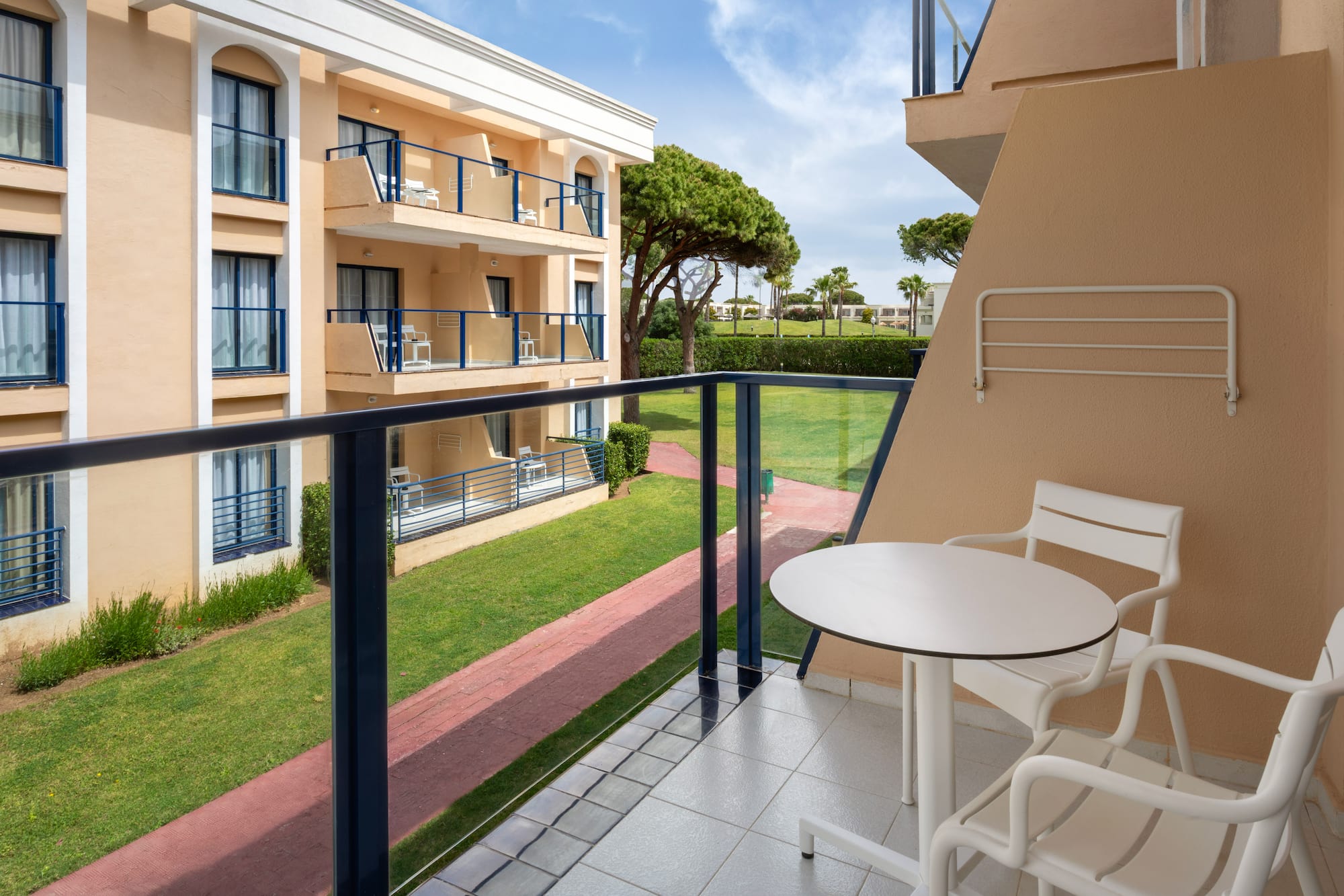 Resort balcony with white outdoor furniture and a lush green garden view.