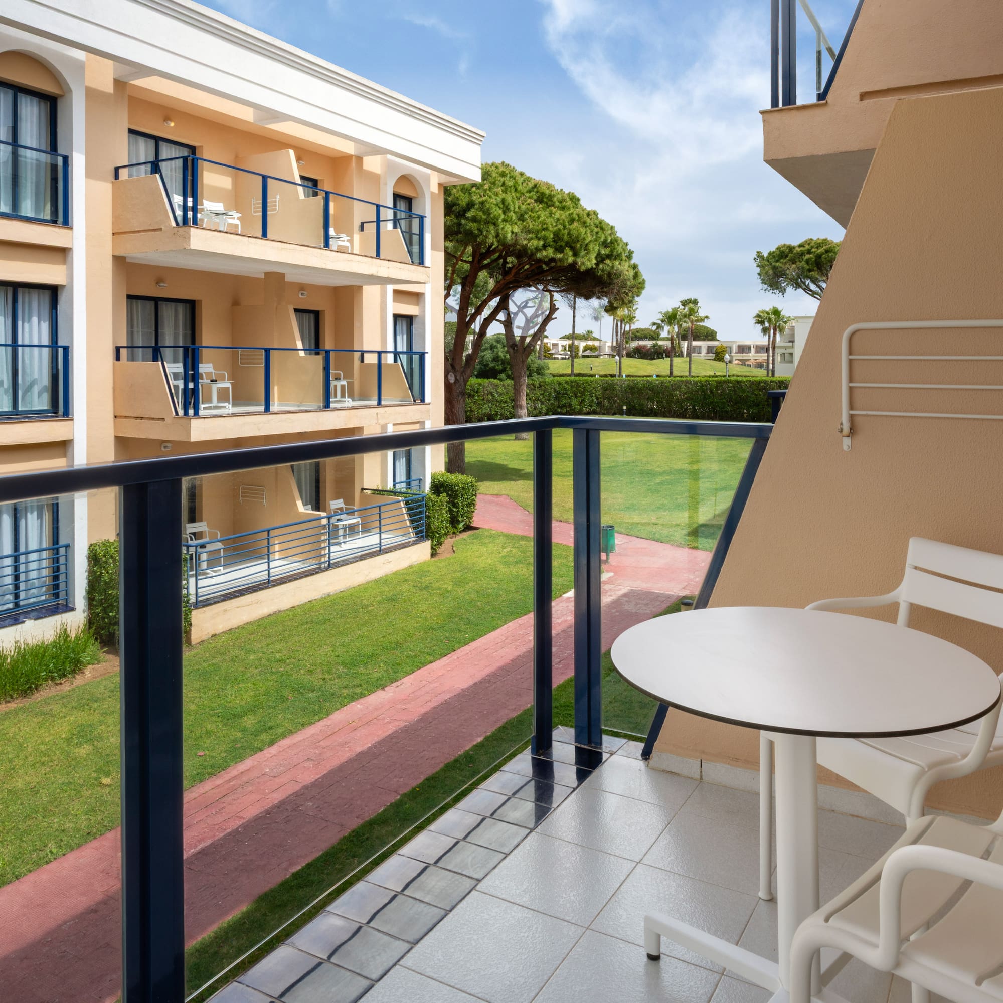 Resort balcony with white outdoor furniture and a lush green garden view.