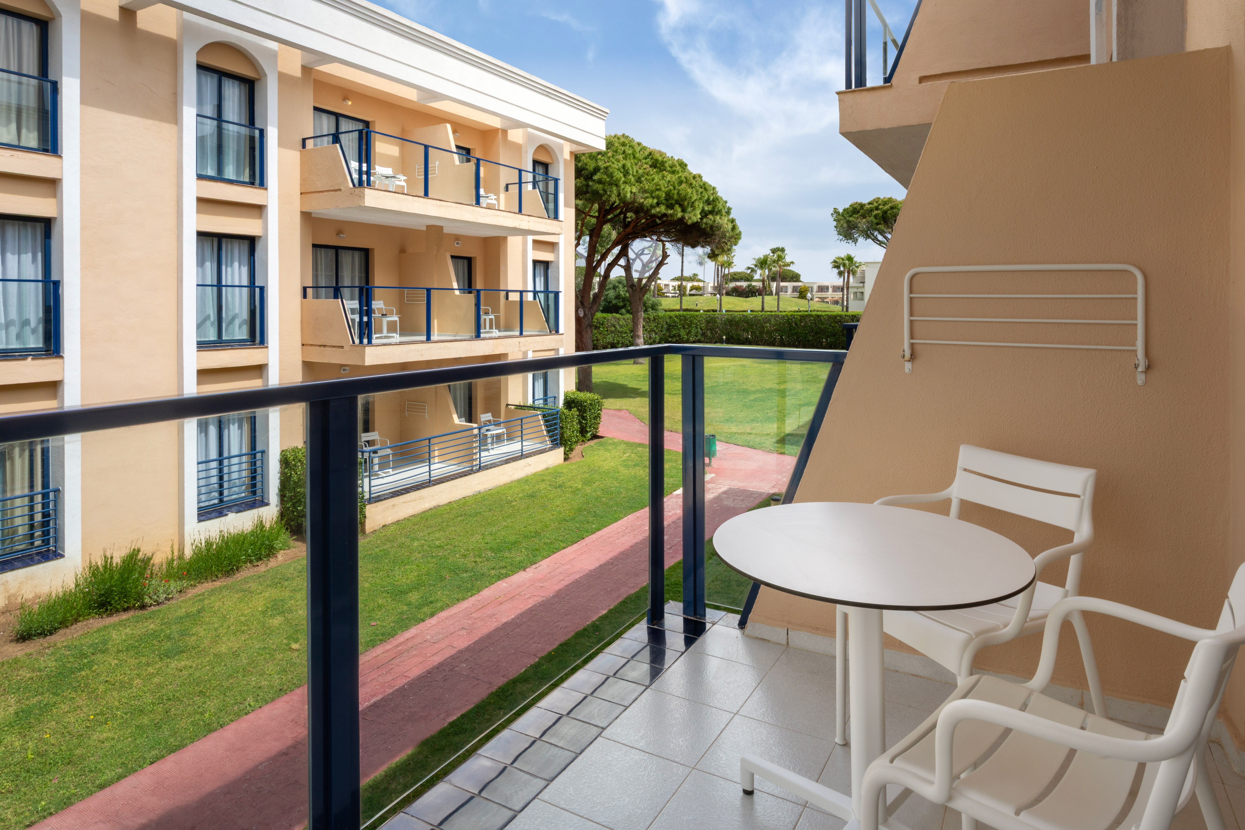 Hotel balcony with outdoor seating, view of resort buildings, and green garden.