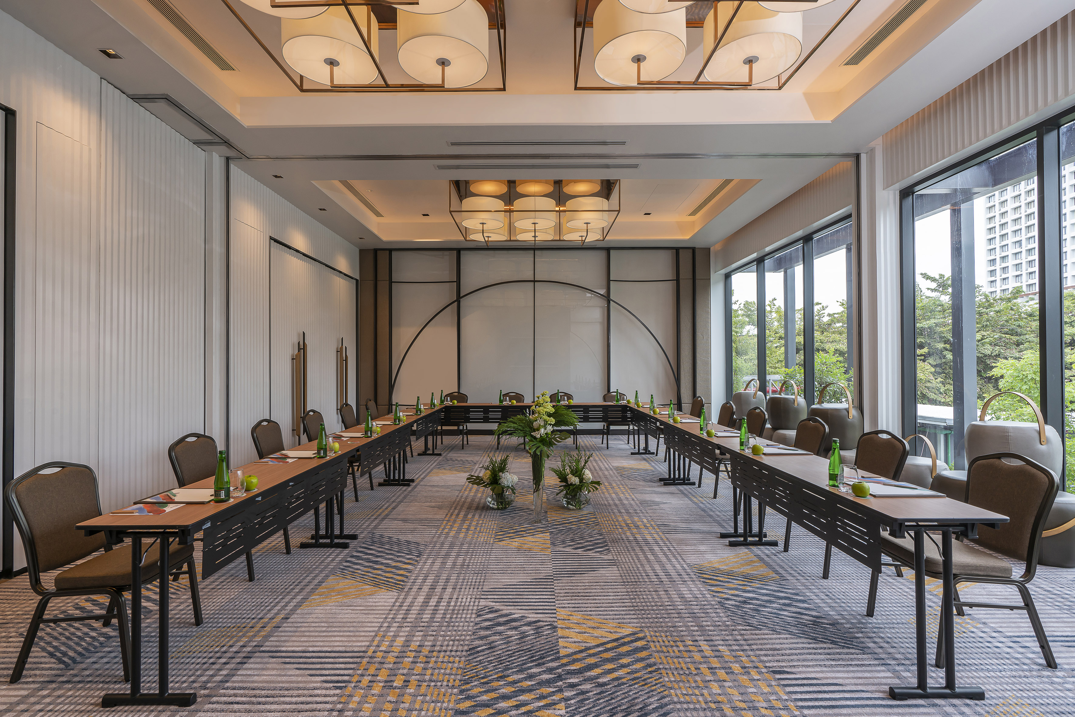 Hotel meeting room with U-shape table, ample natural light, and modern decor.