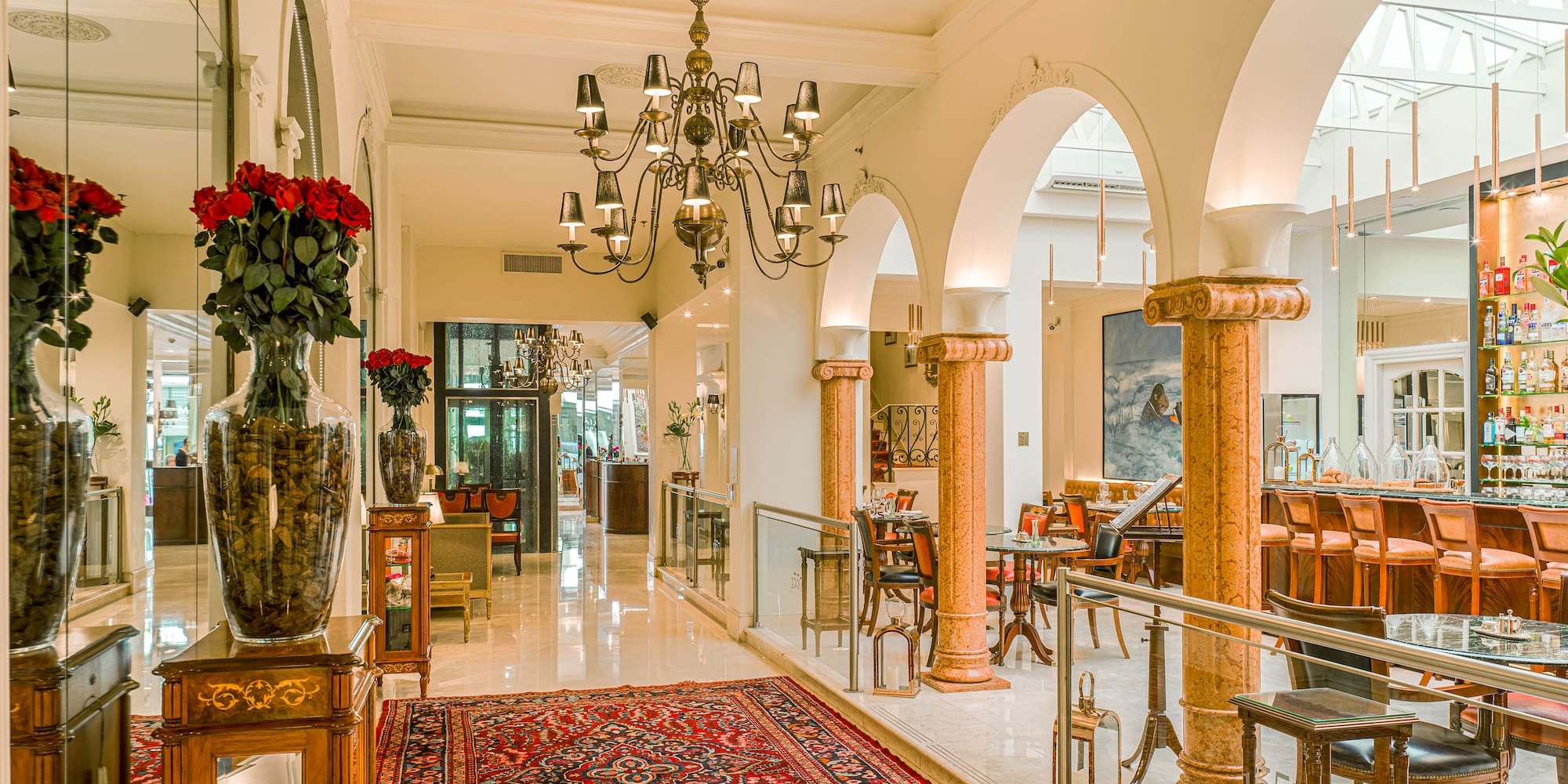 Luxurious hotel lounge with a grand chandelier, red patterned rug, and a chic bar.
