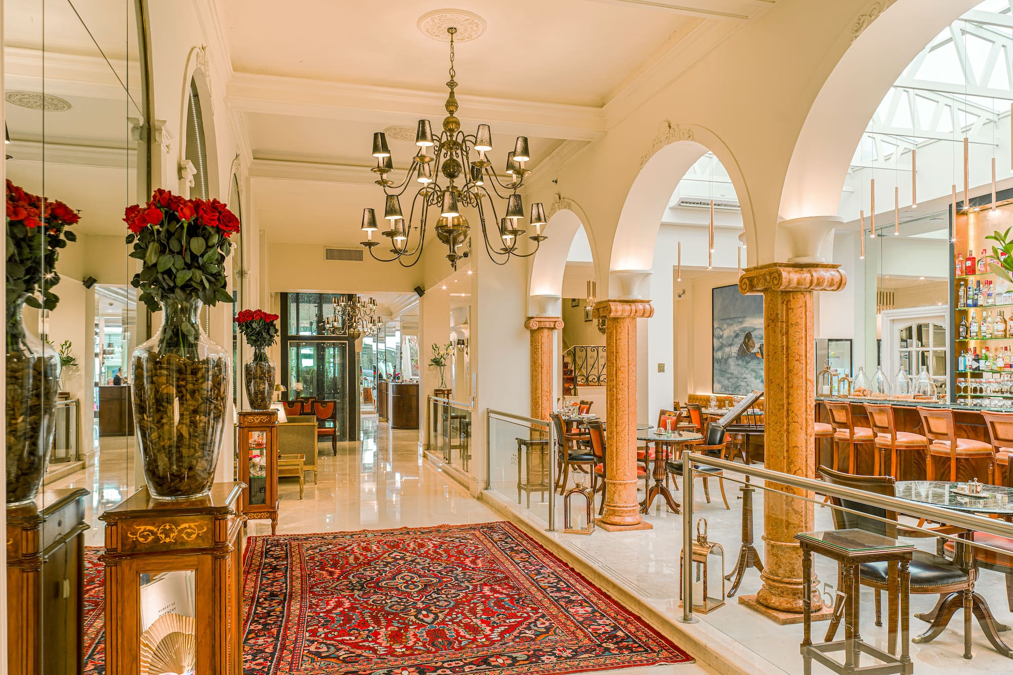 Luxurious hotel lounge with a grand chandelier, red patterned rug, and a chic bar.