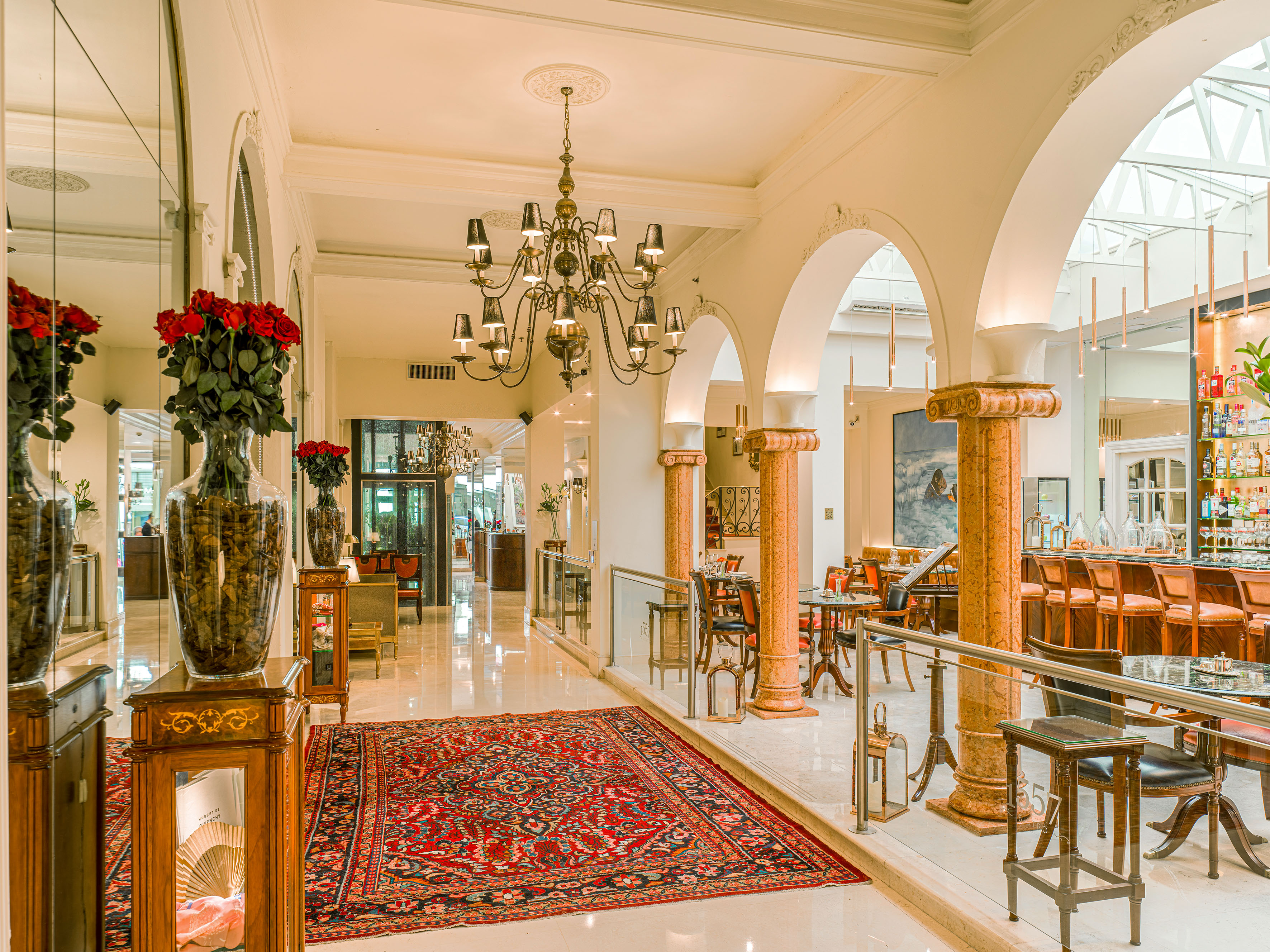 Luxurious hotel lounge with a grand chandelier, red patterned rug, and a chic bar.