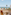 Beachfront patio with two chairs, ocean view, palm trees, and straw huts.