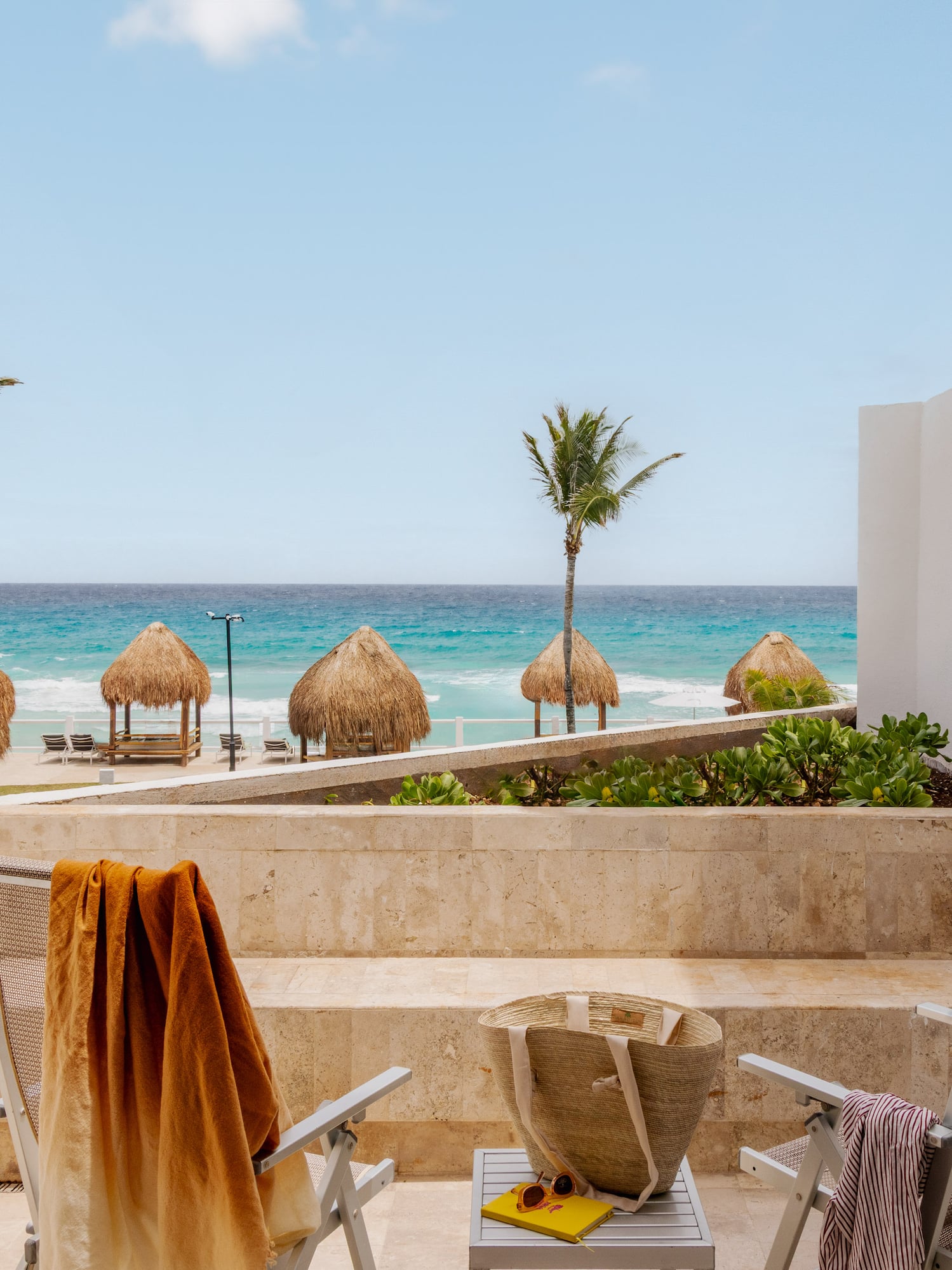 Beachfront patio with two chairs, ocean view, palm trees, and straw huts.