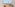 Oceanfront balcony view of tropical beach with palapas, palm trees, and chairs.