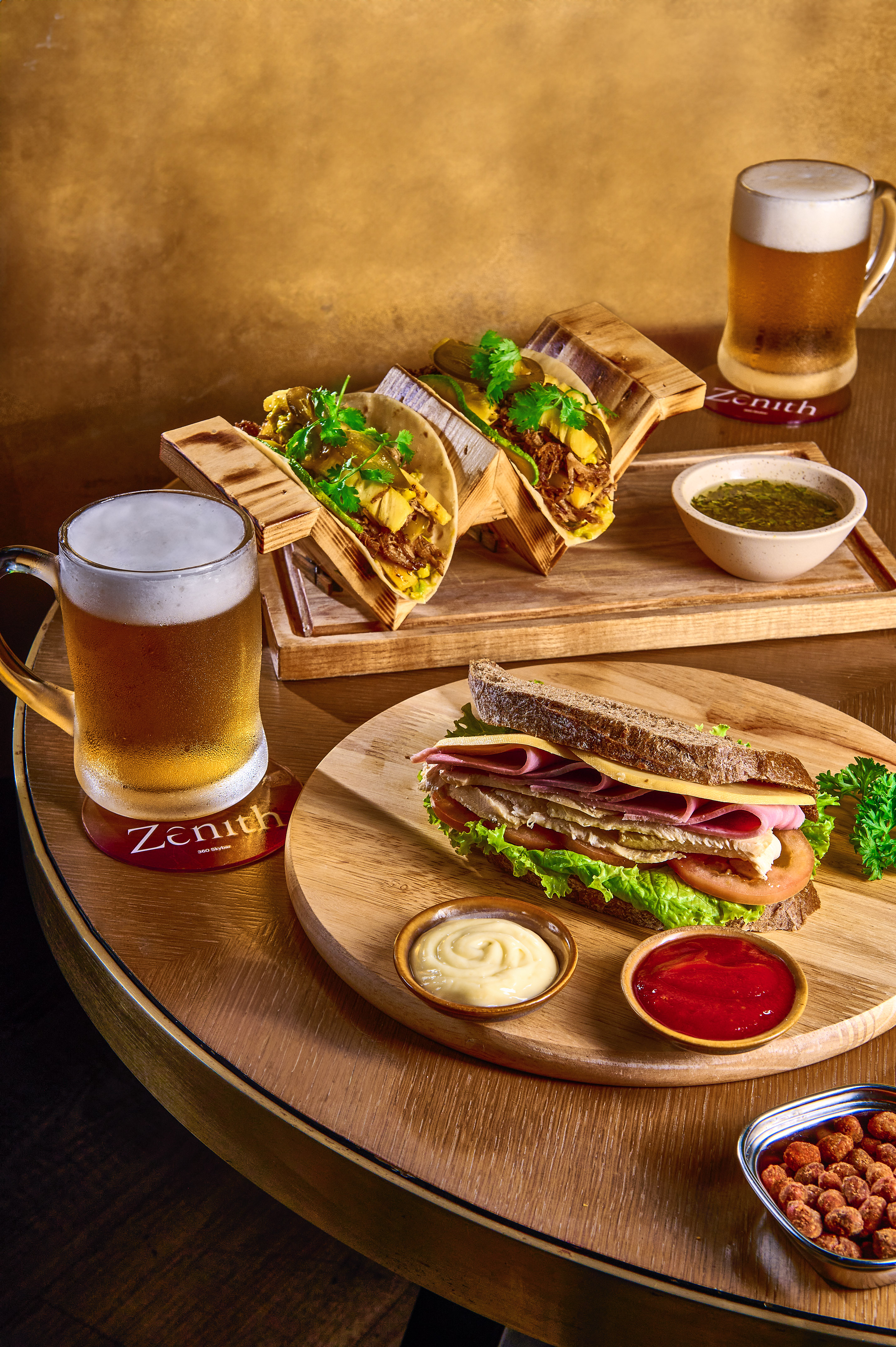 Zenith bar: Beers, loaded tacos, and club sandwich on wooden table.