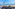 Chairs on wooden balcony overlooking calm sea, palm trees, and distant islands.