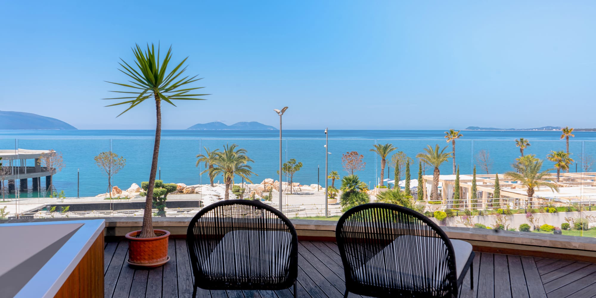 Chairs on wooden balcony overlooking calm sea, palm trees, and distant islands.