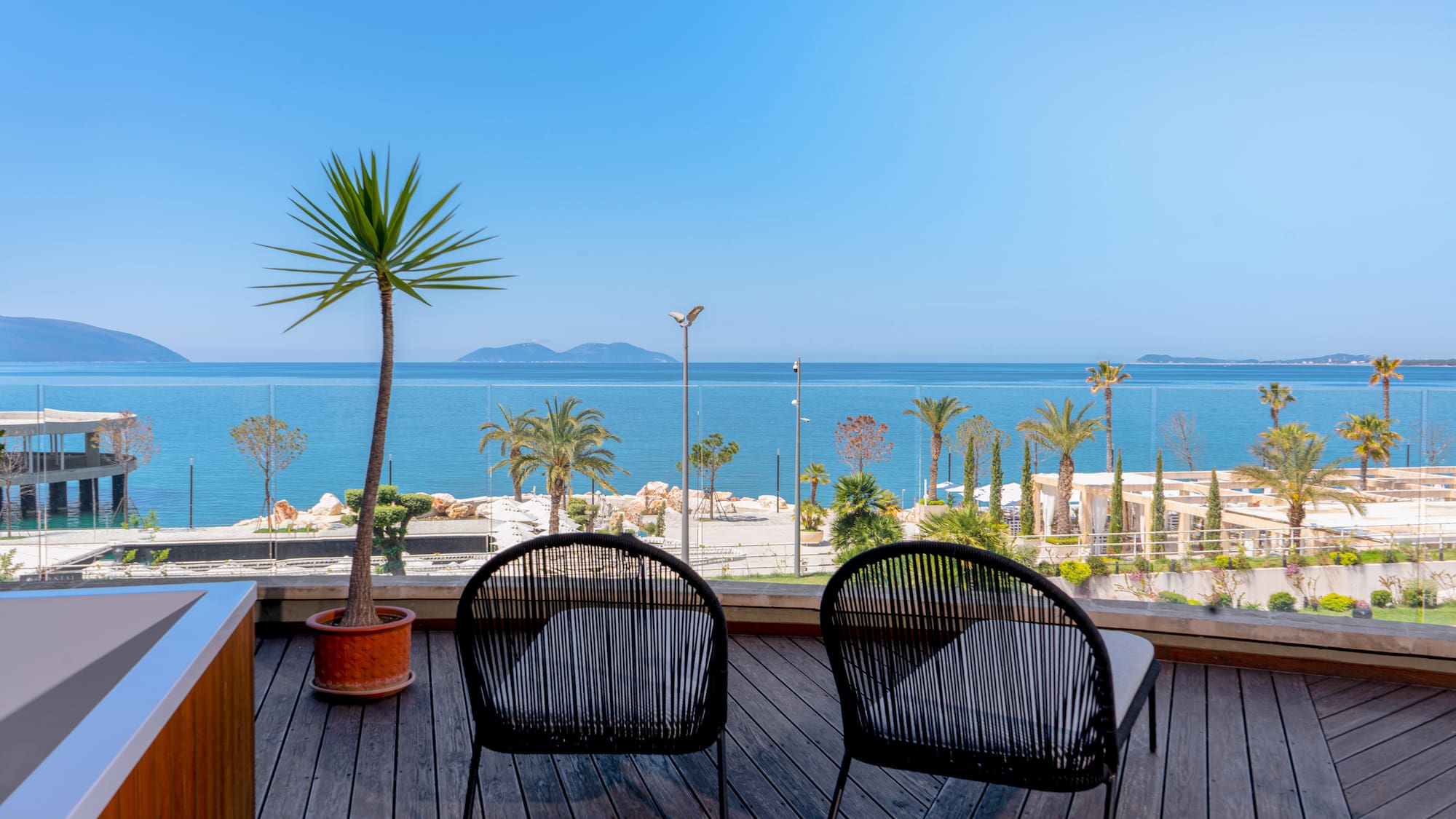 Chairs on wooden balcony overlooking calm sea, palm trees, and distant islands.