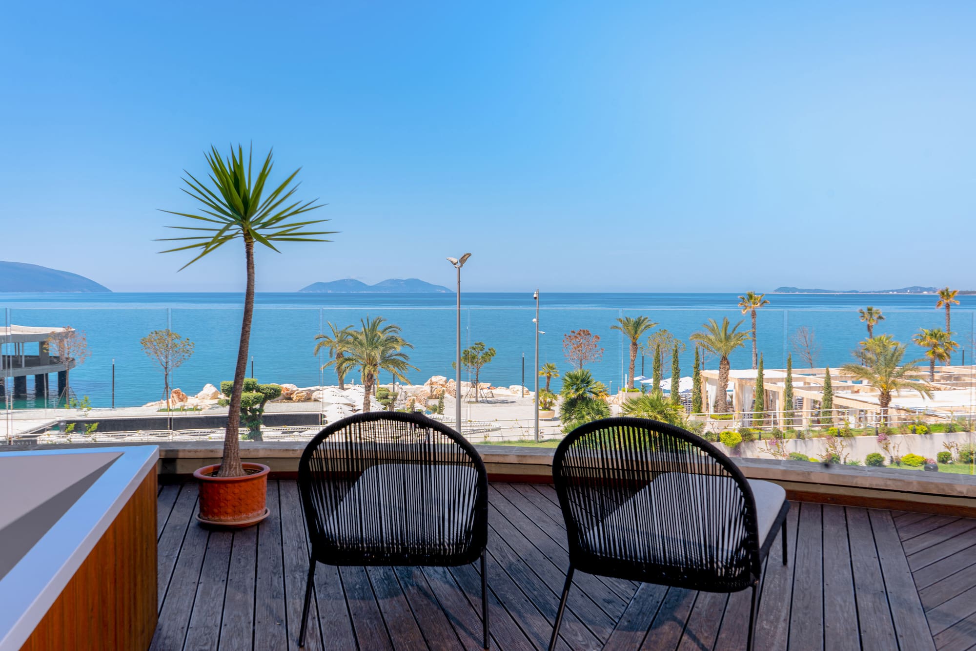Chairs on wooden balcony overlooking calm sea, palm trees, and distant islands.