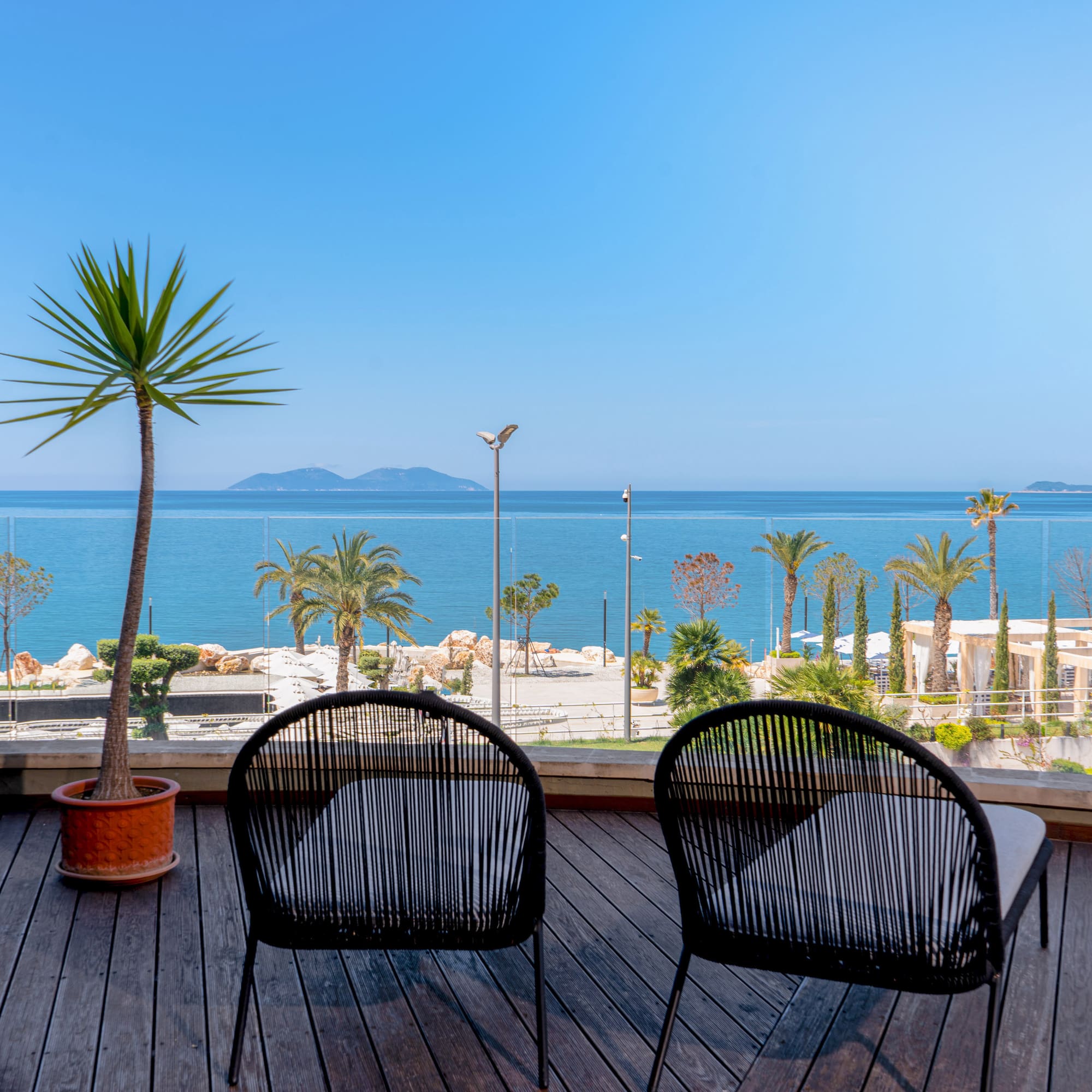 Chairs on wooden balcony overlooking calm sea, palm trees, and distant islands.