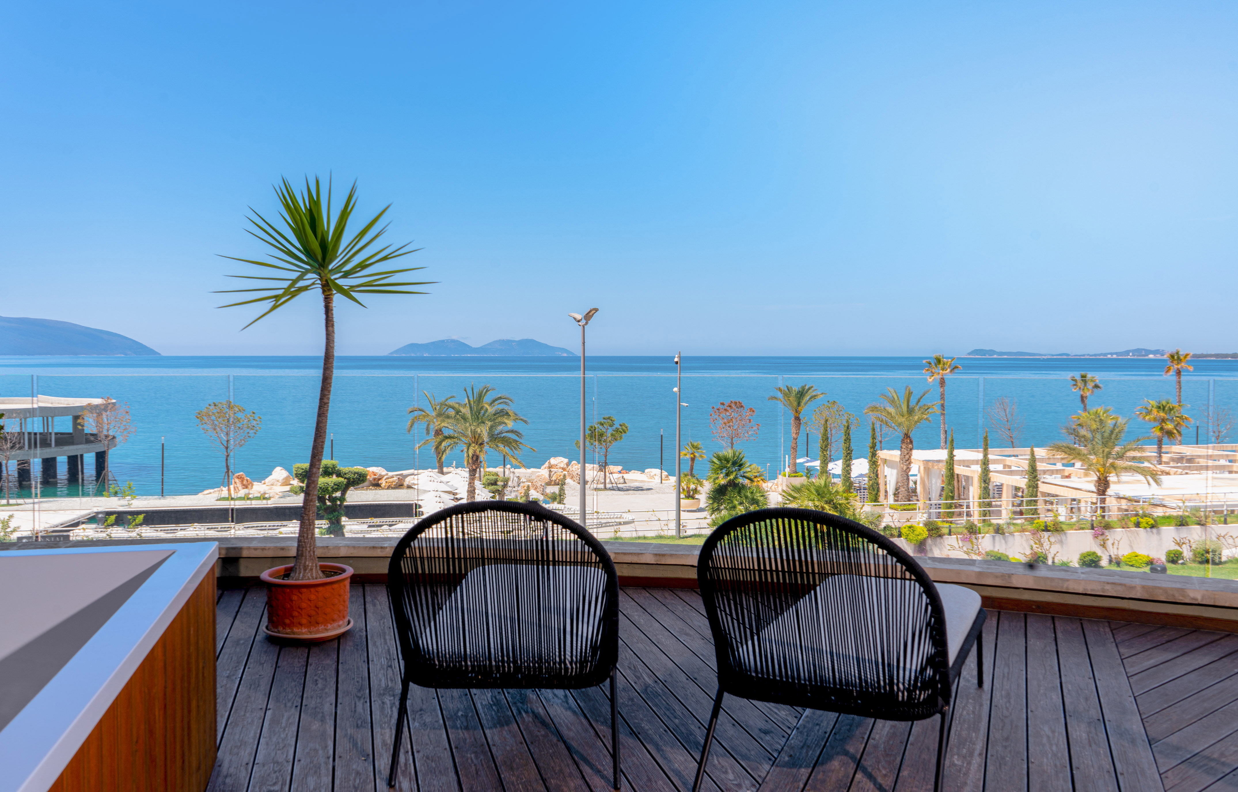 Chairs on wooden balcony overlooking calm sea, palm trees, and distant islands.