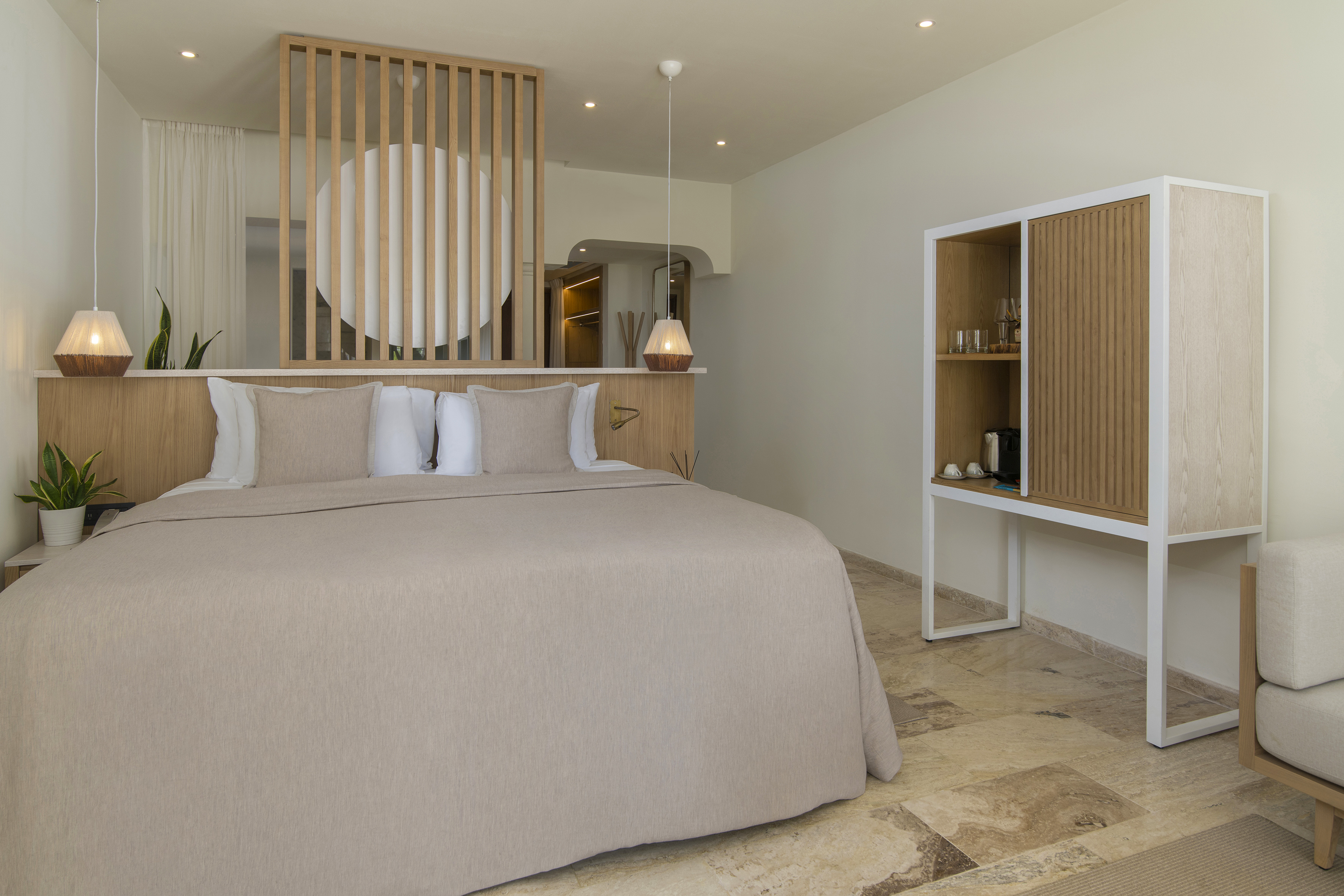 Neutral modern hotel bedroom with king bed, wooden screen, and minibar cabinet.