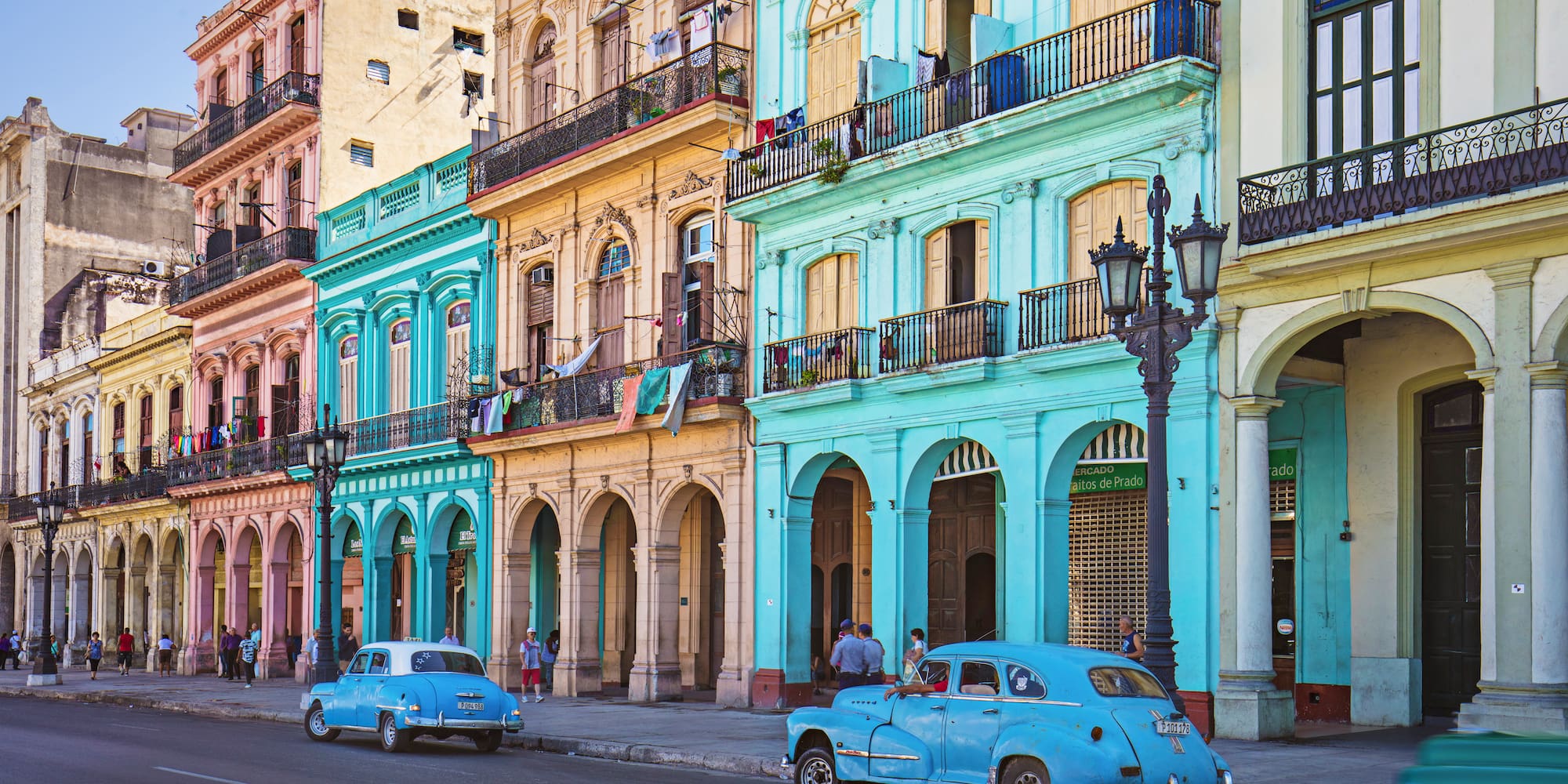 a blue car on a street with buildings and people
