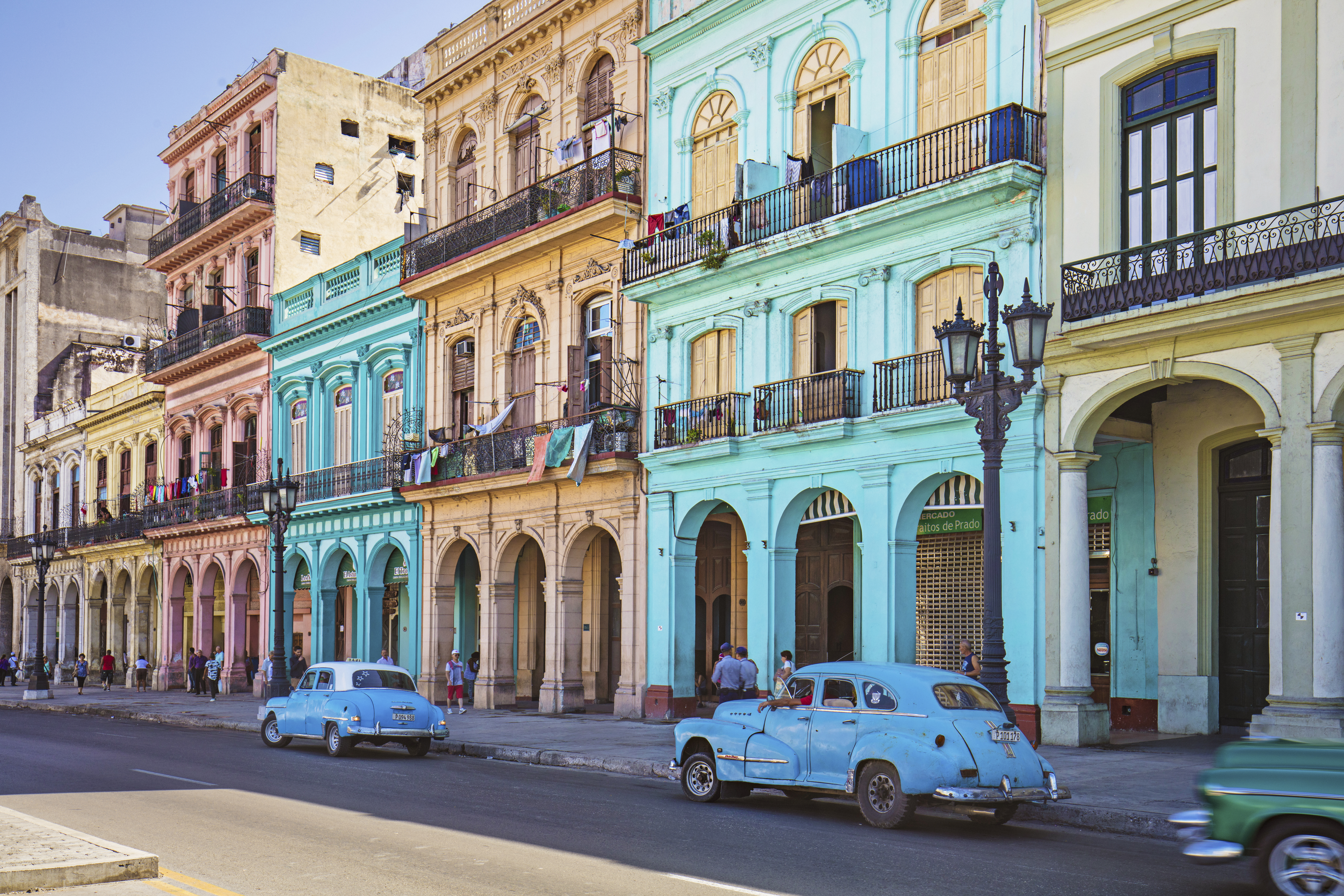 a blue car on a street with buildings and people