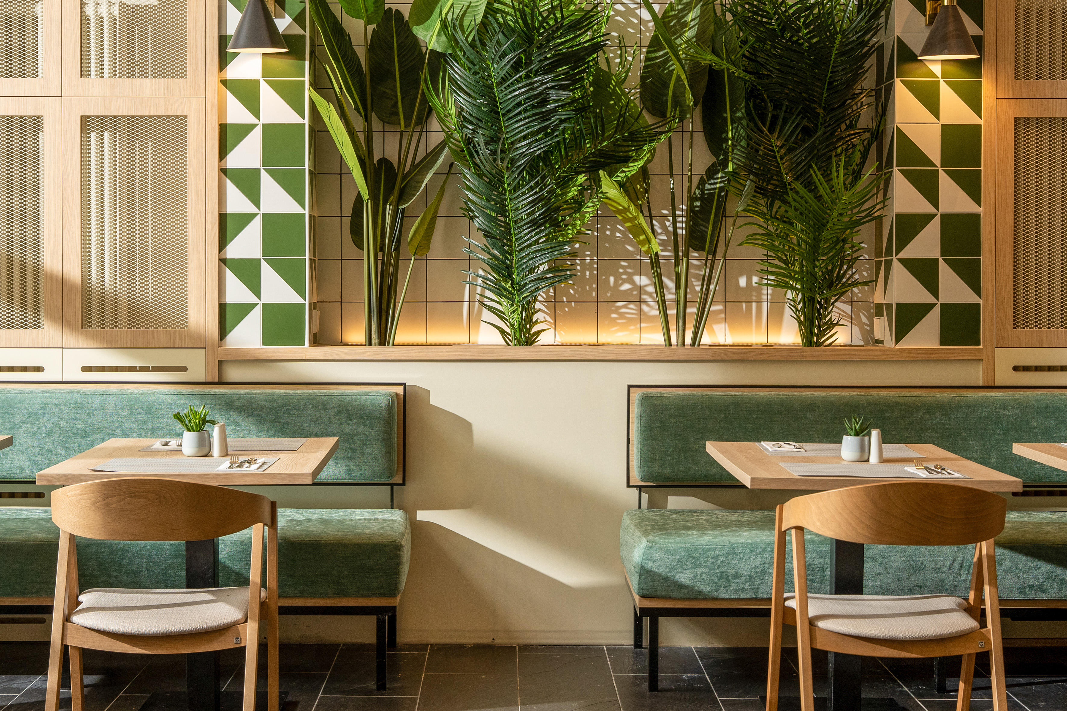 Cafe interior: green booths, wood tables, lush plants, and geometric wall tiles.