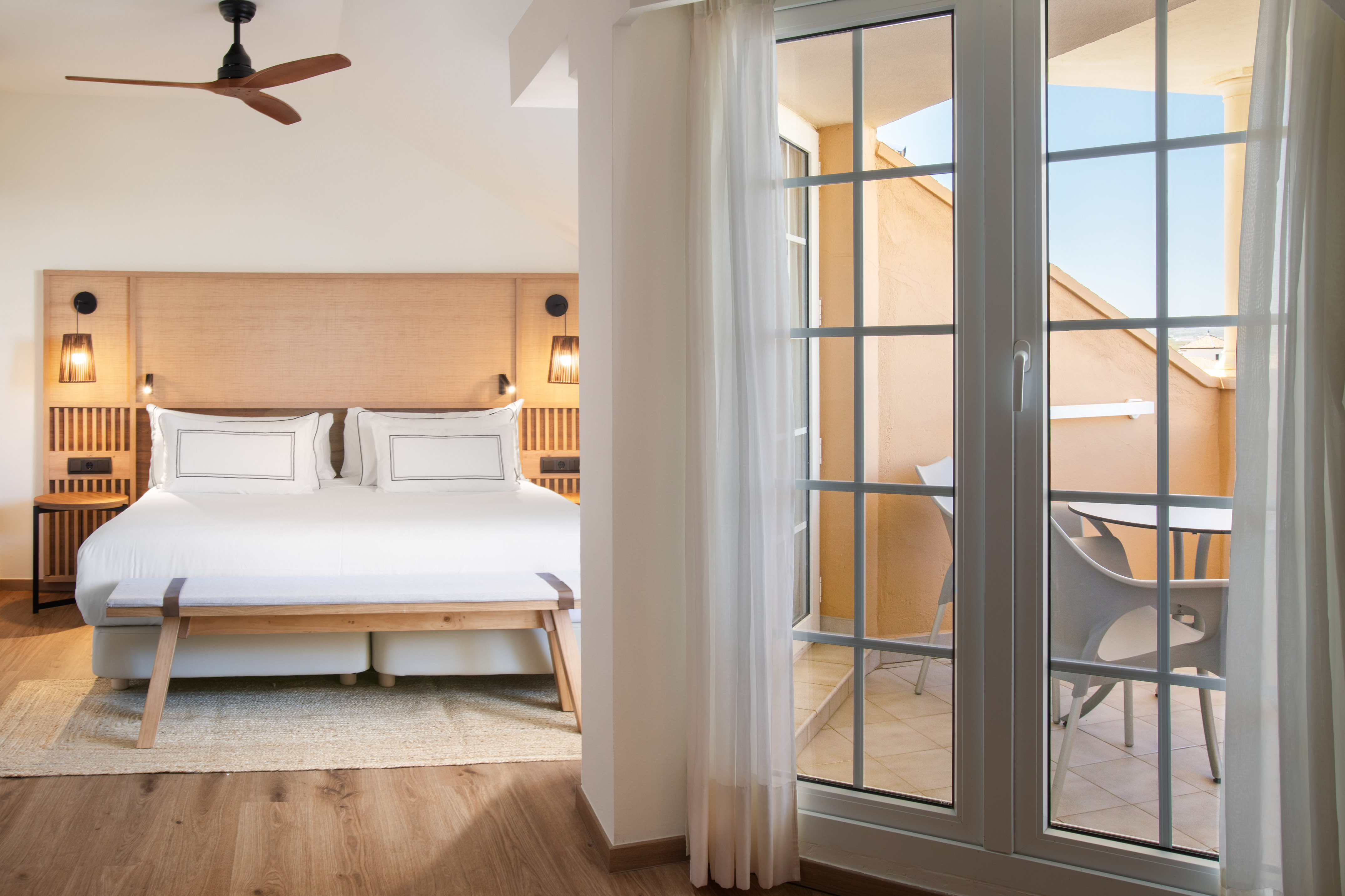 Modern hotel bedroom with king bed, wooden headboard, and sunny balcony.