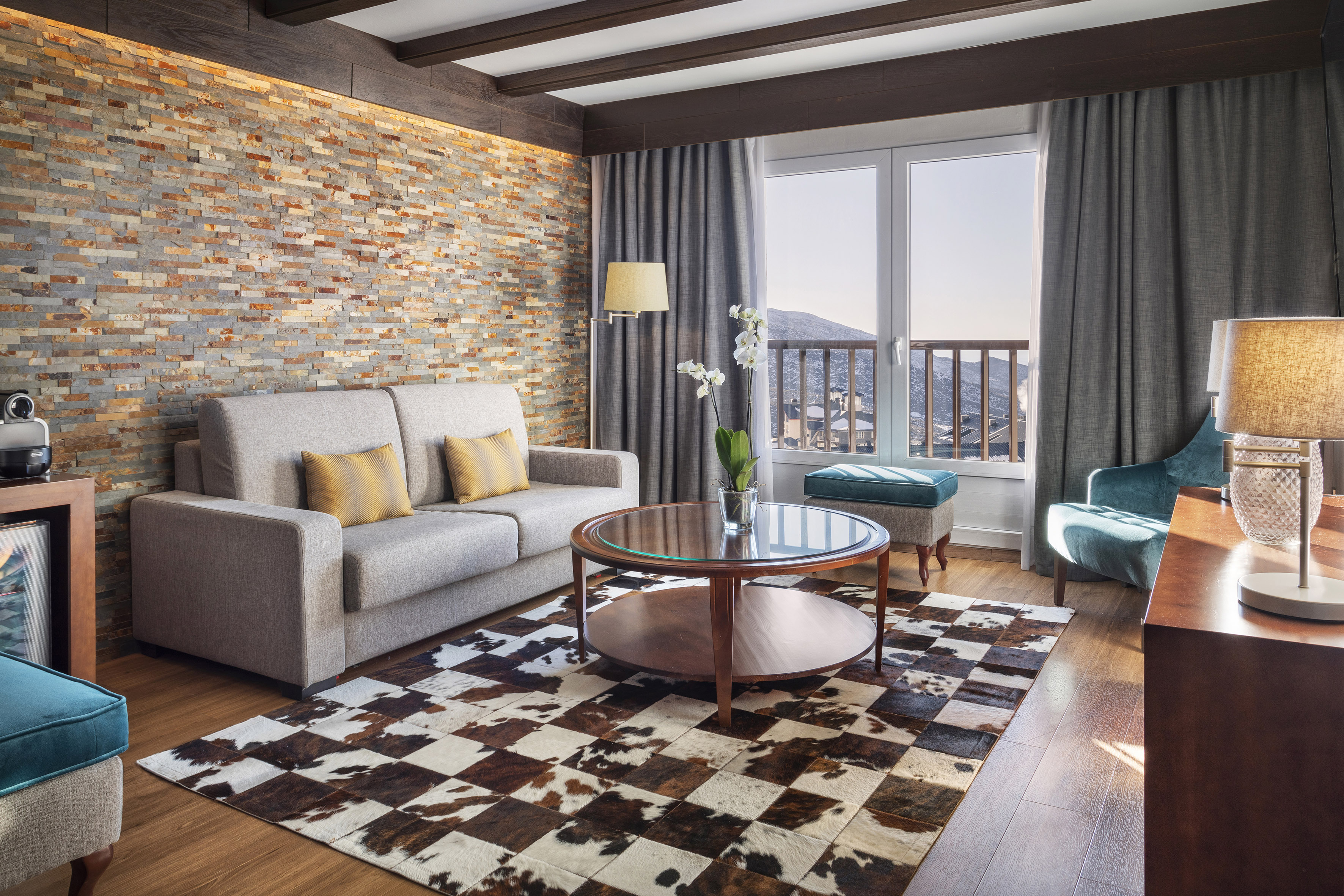 Cozy hotel living room with stone wall, sofa, cowhide rug, and mountain view.