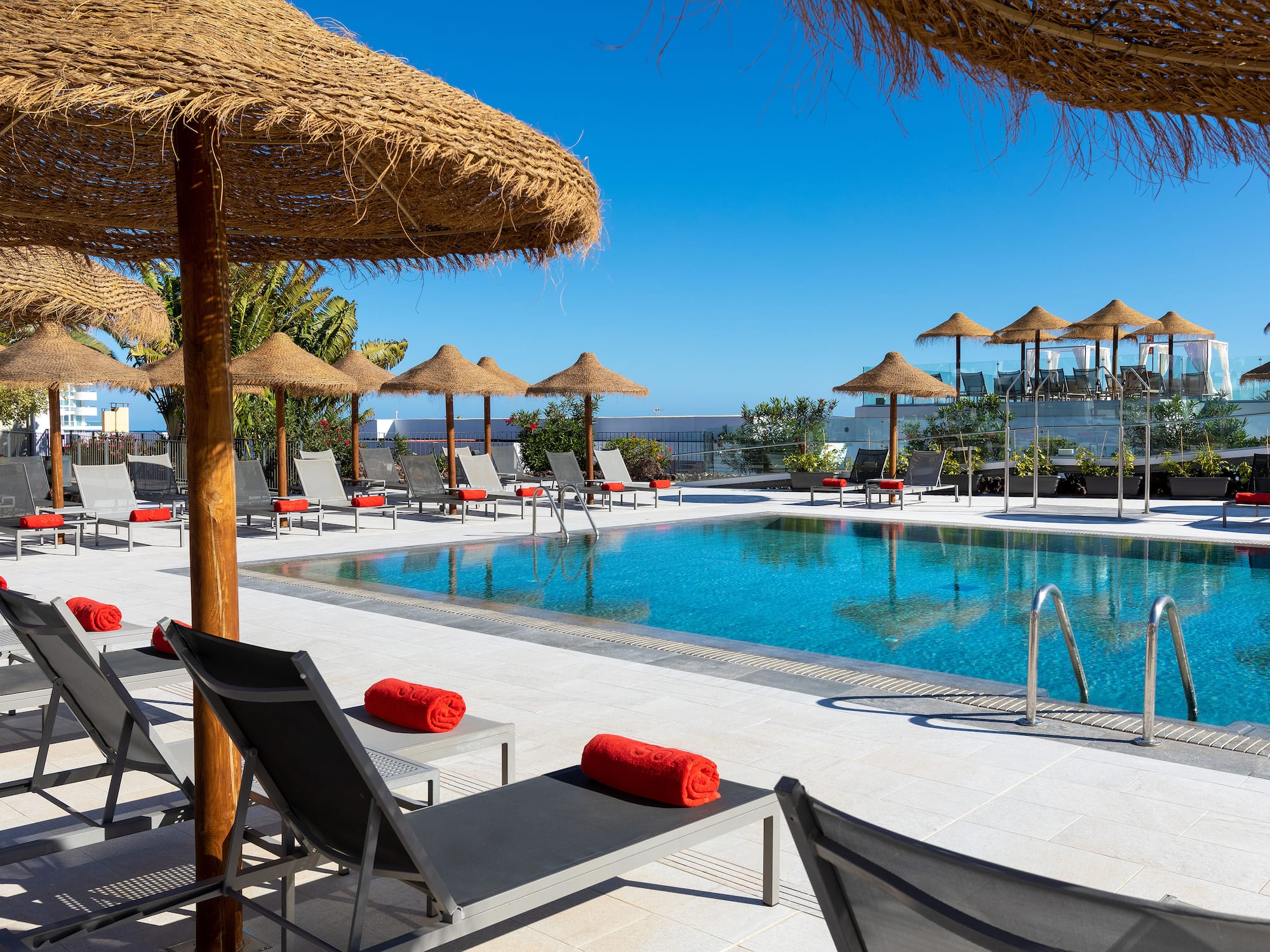 a pool with straw umbrellas and lounge chairs