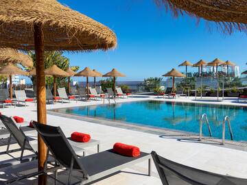 a pool with straw umbrellas and lounge chairs