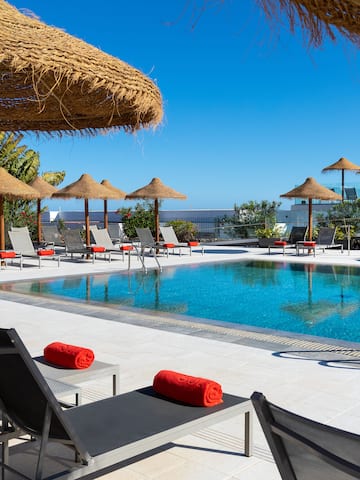 a pool with straw umbrellas and lounge chairs