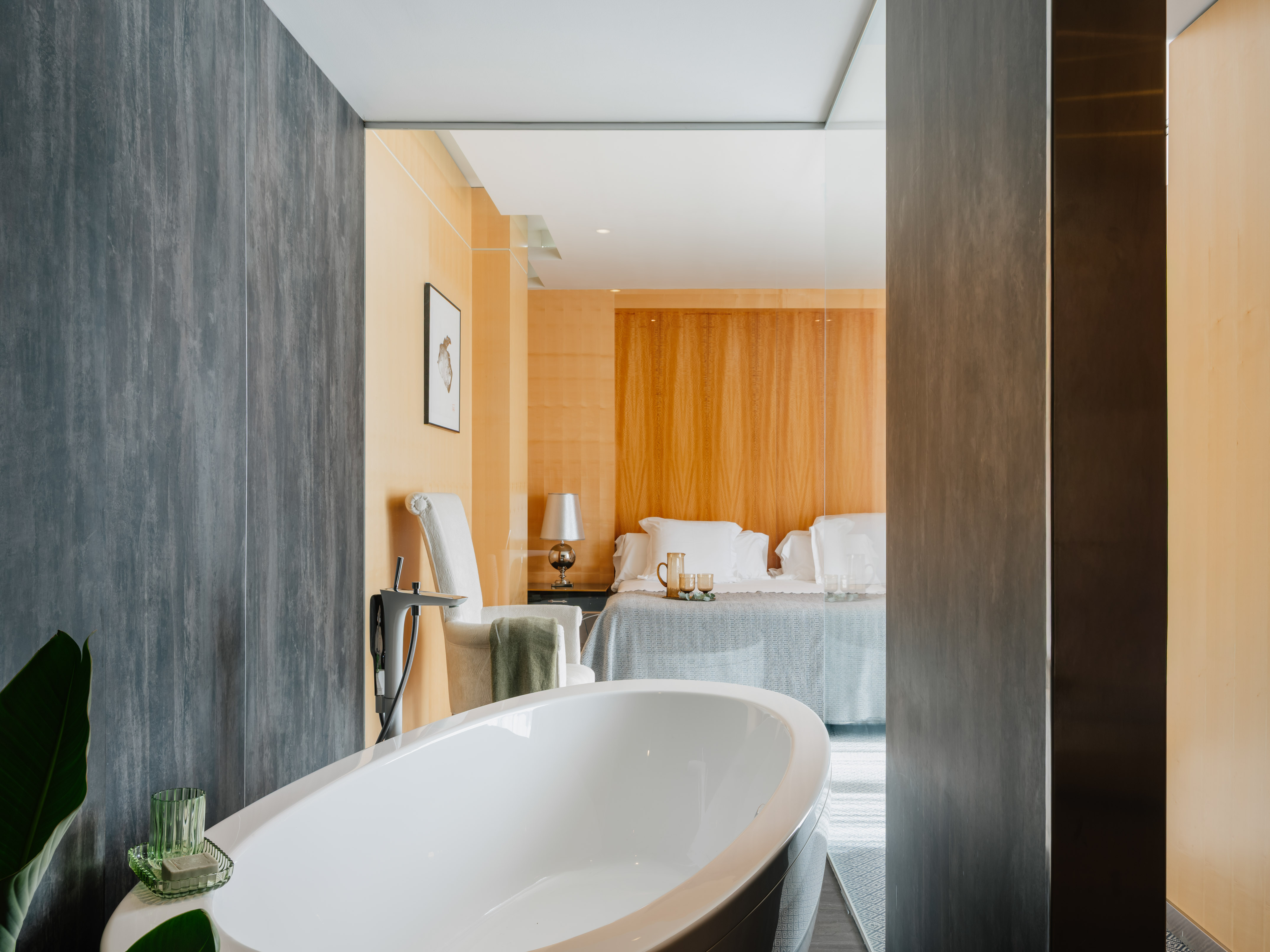 Modern hotel suite with freestanding tub and open-plan bedroom.