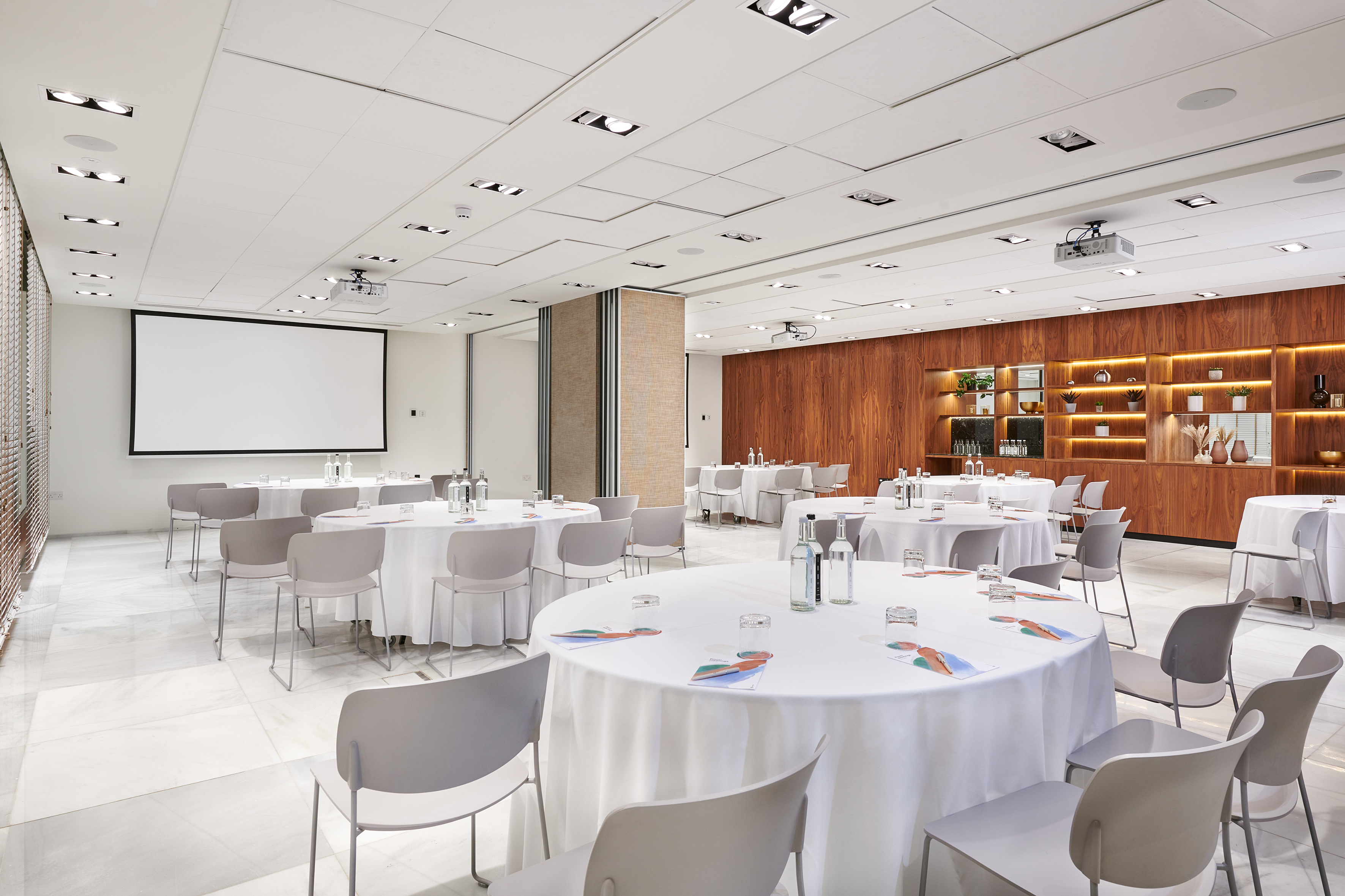 Modern conference room with round tables, projector screen, and wooden feature wall.