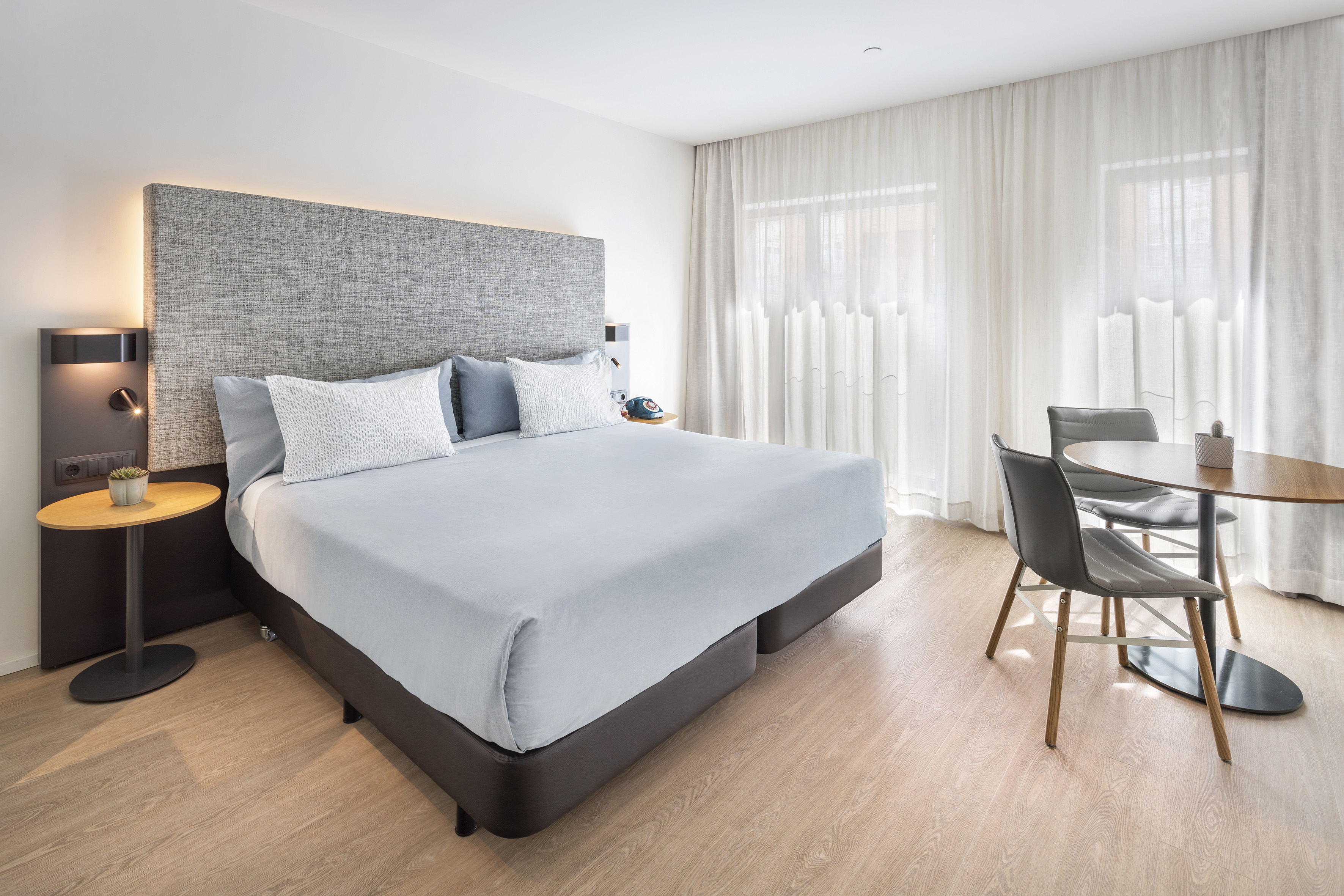 Modern hotel room with king bed, light blue bedding, and dining area.