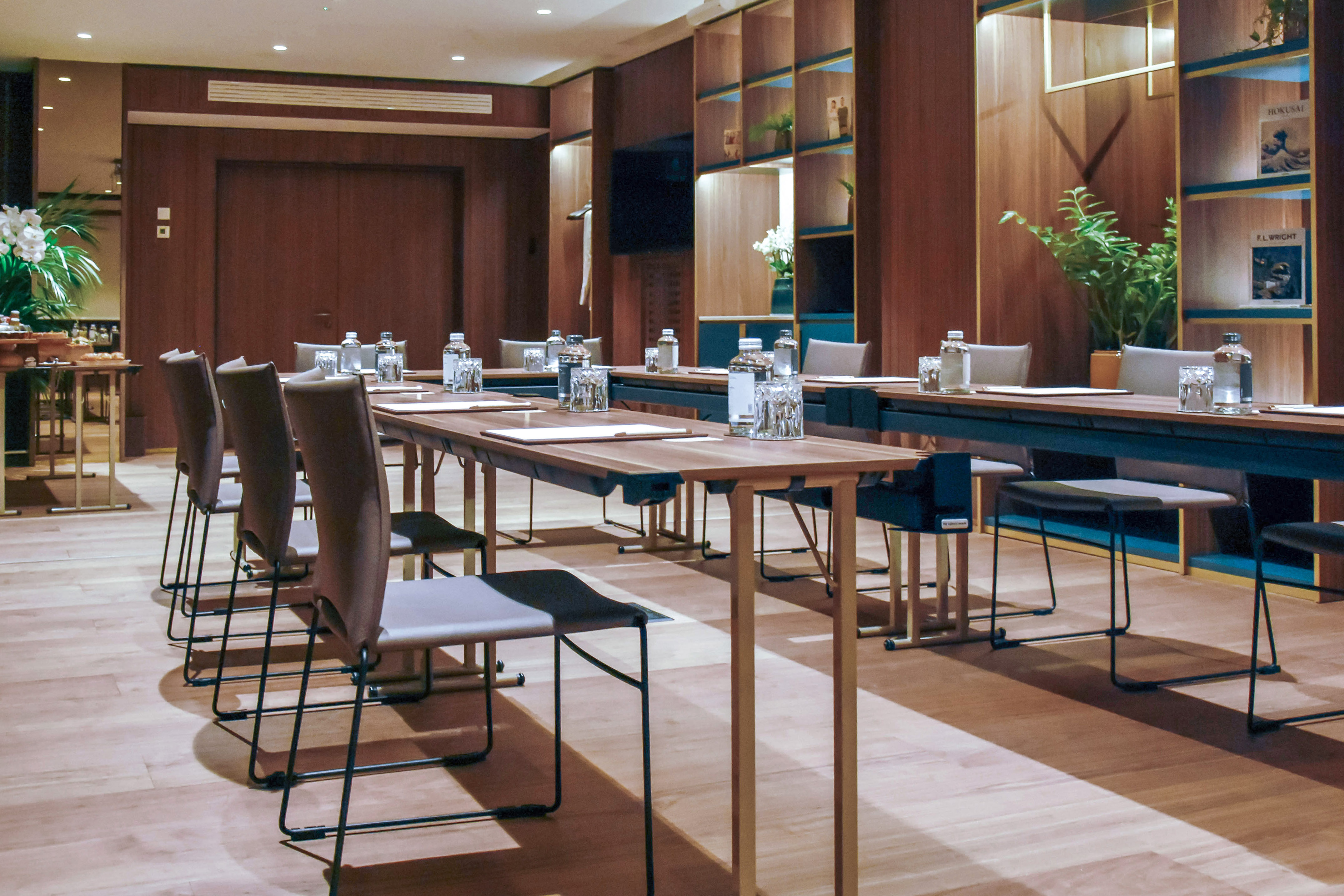 Modern meeting room with wooden tables, chairs, water bottles, and warm lighting.