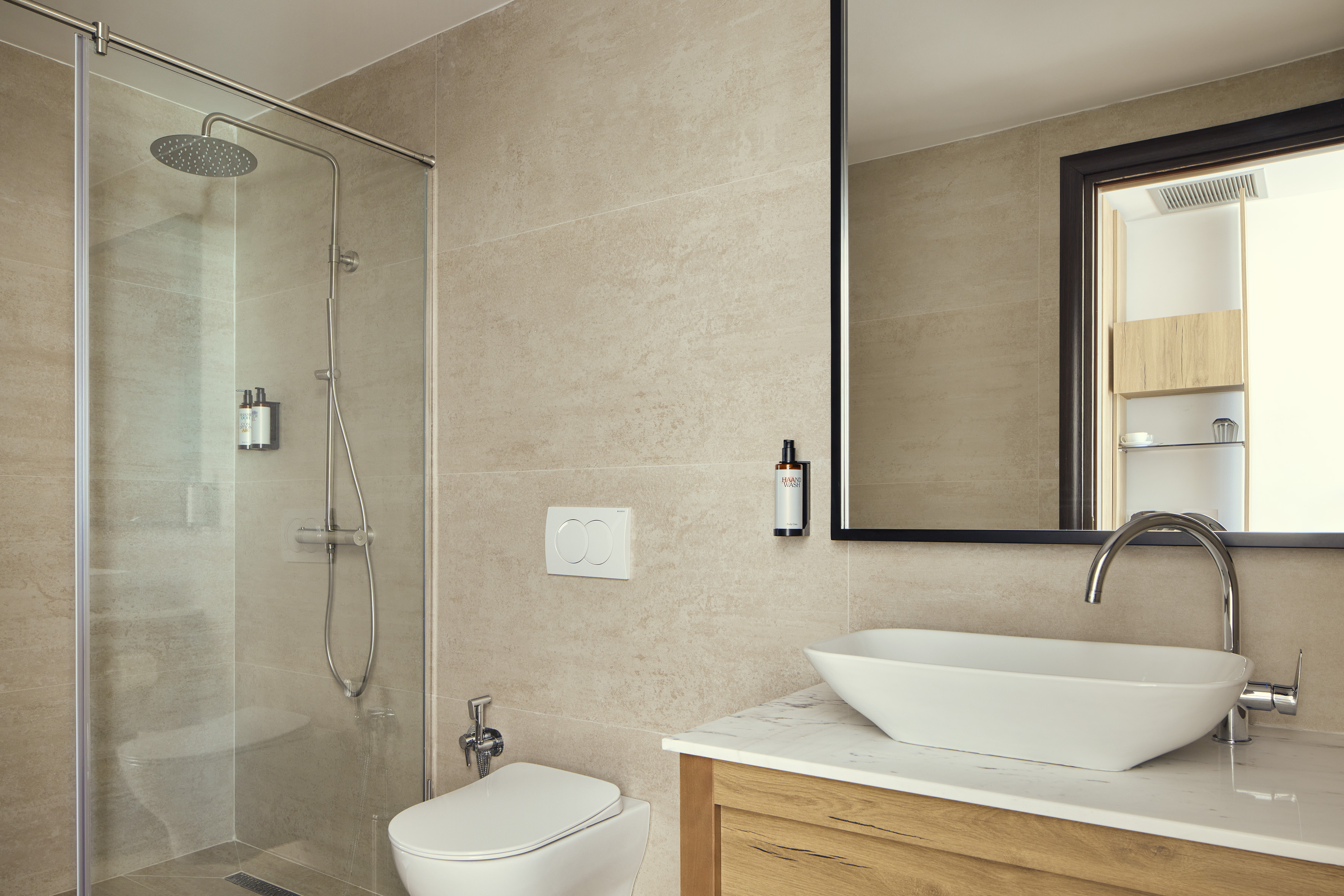 Beige tiled modern bathroom with glass shower, toilet, and sleek vanity.