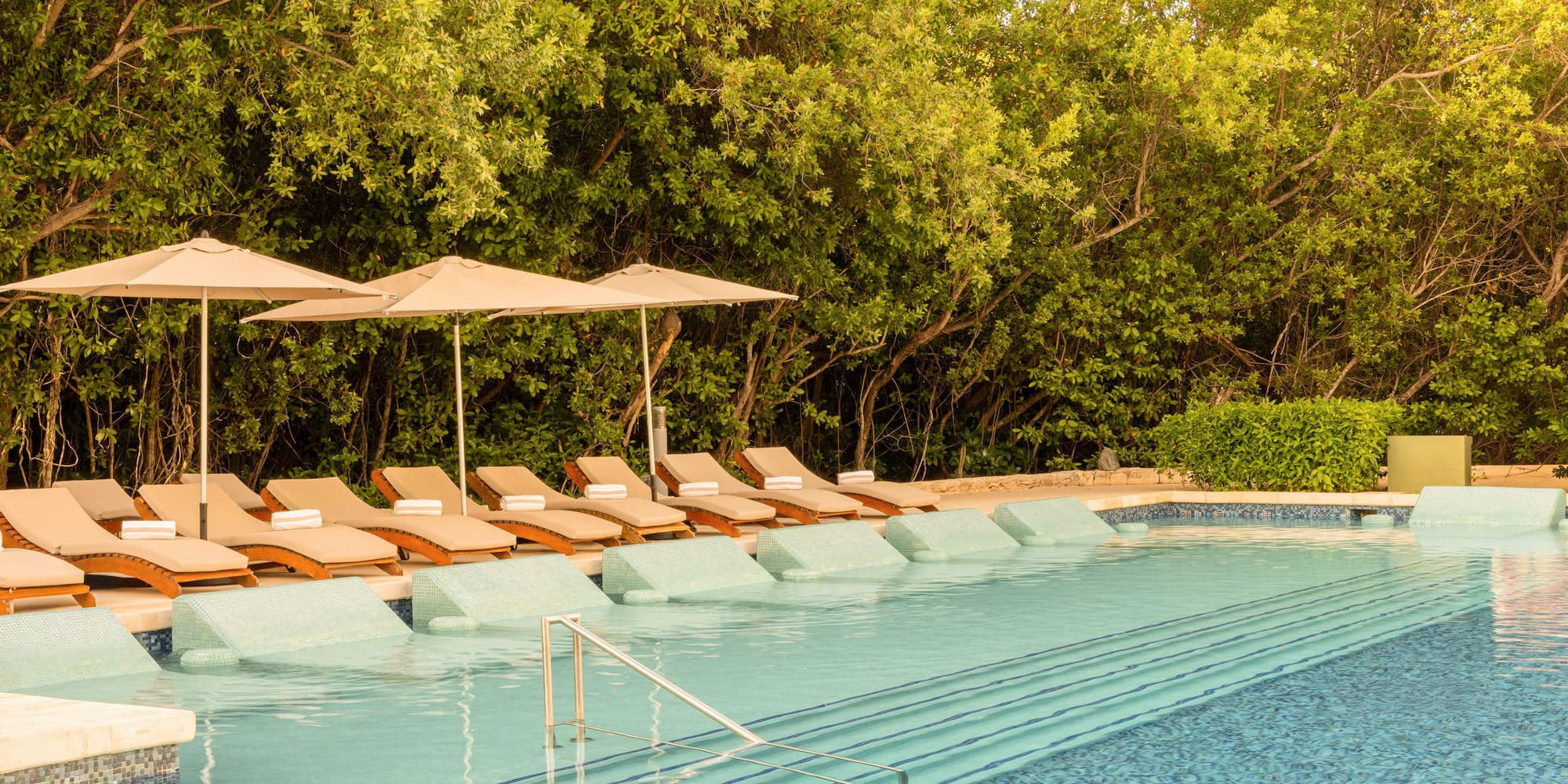 Luxury resort pool with in-pool loungers, umbrellas, and lush tropical trees.