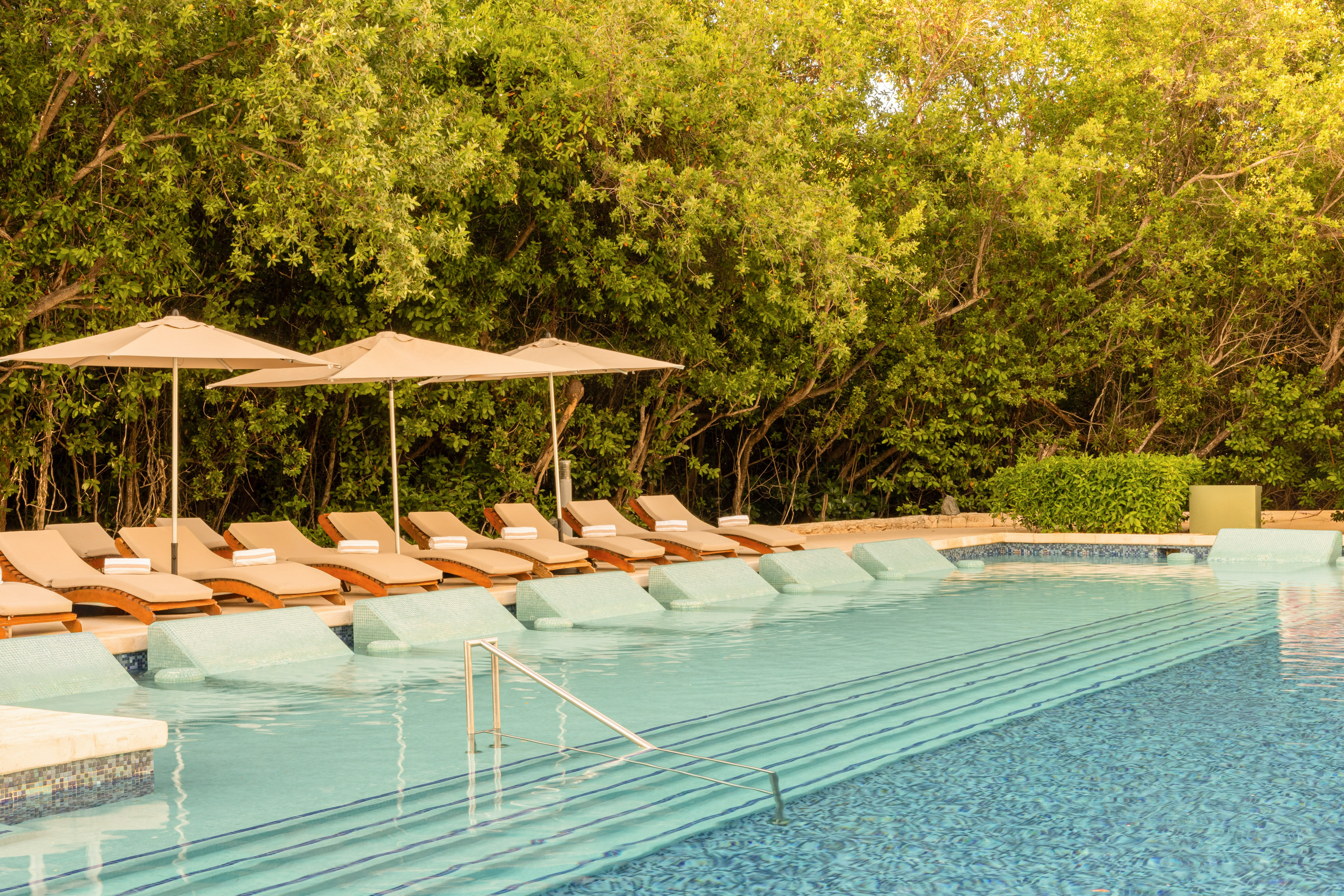 Luxury resort pool with in-pool loungers, umbrellas, and lush tropical trees.