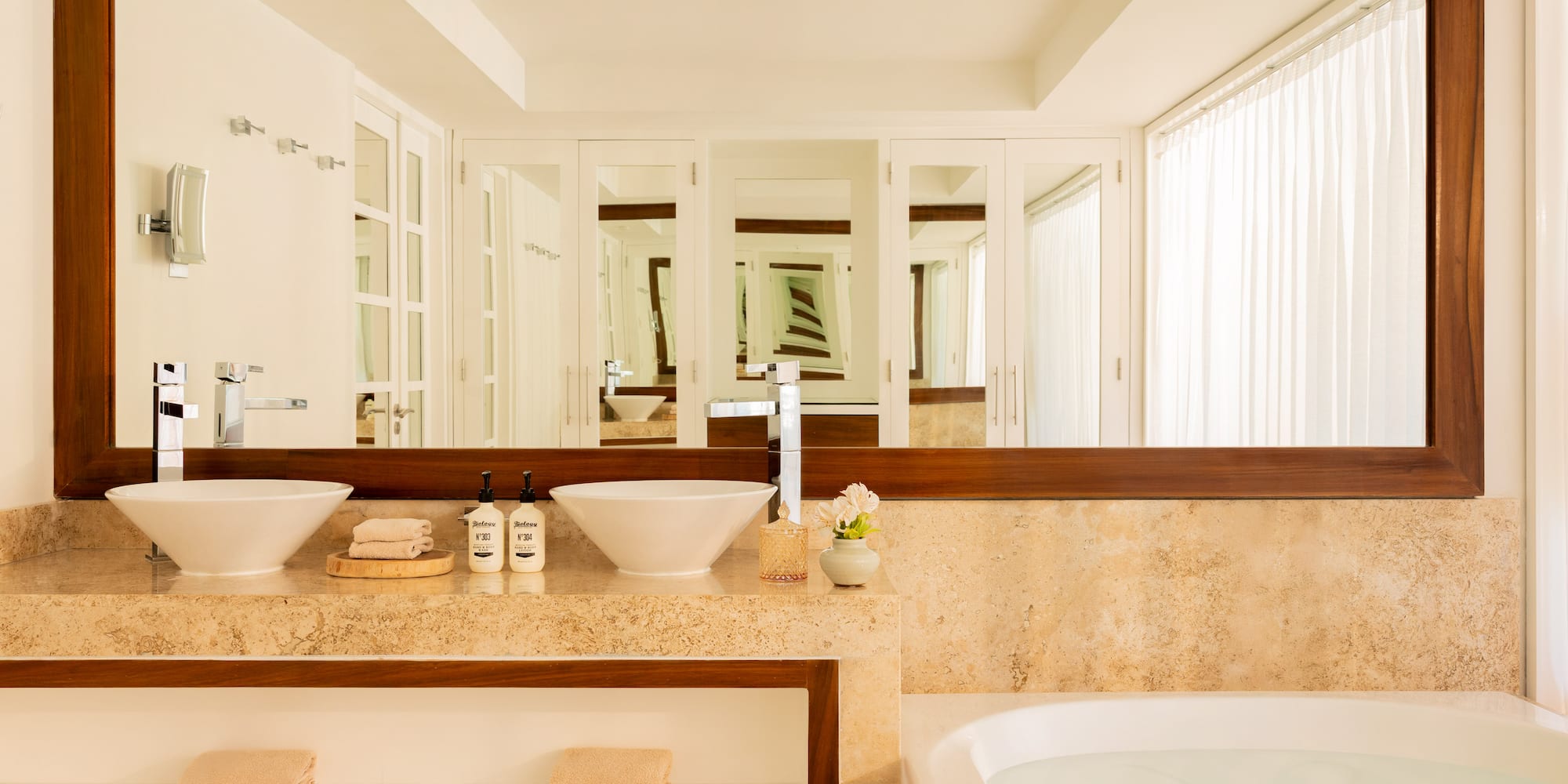 Modern bathroom with double vessel sinks, marble vanity, large mirror, and bathtub.