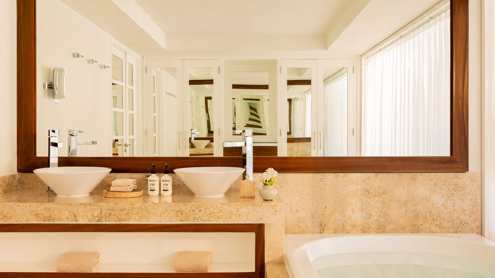 Modern bathroom with double vessel sinks, marble vanity, large mirror, and bathtub.