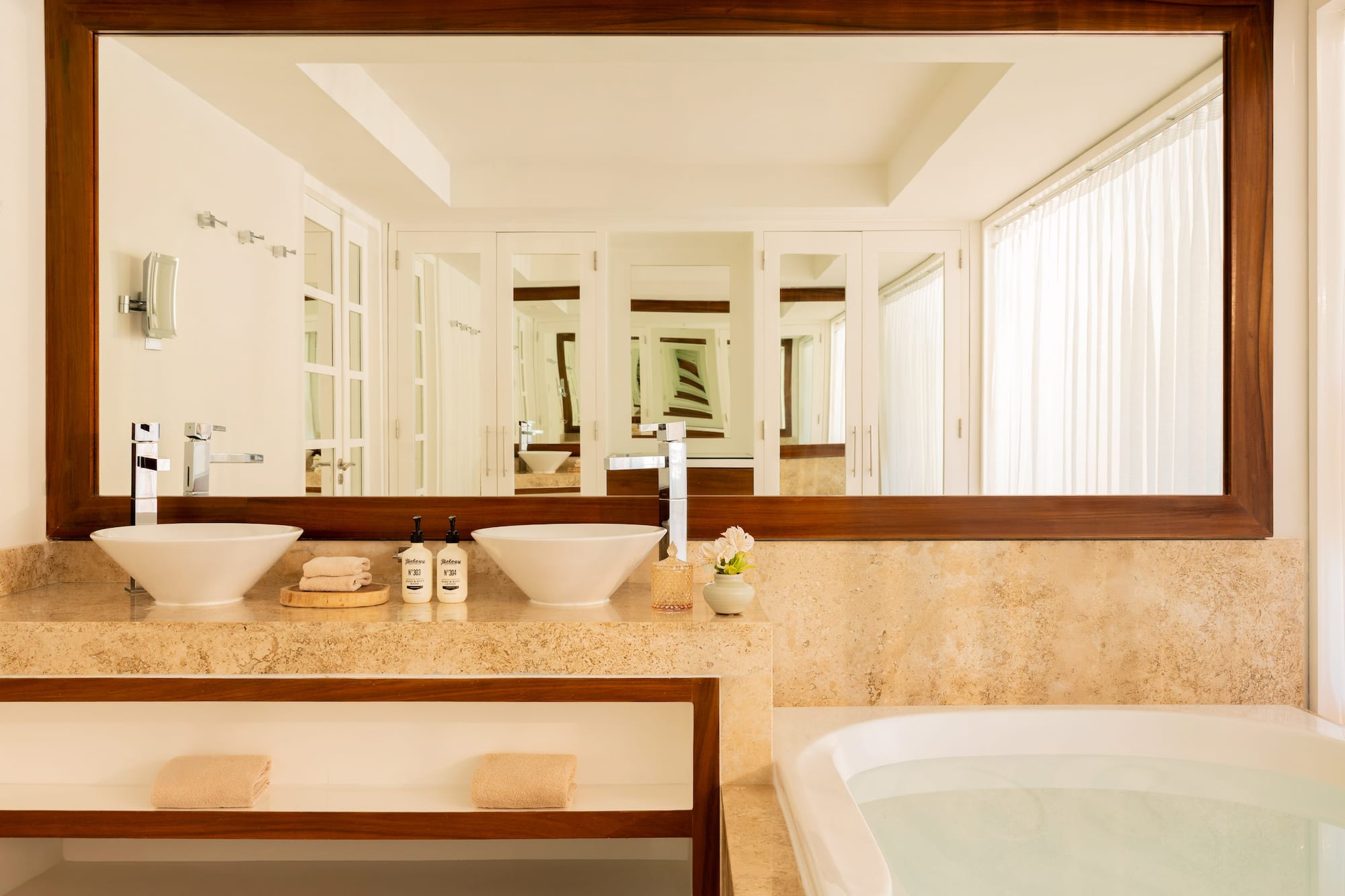 Modern bathroom with double vessel sinks, marble vanity, large mirror, and bathtub.