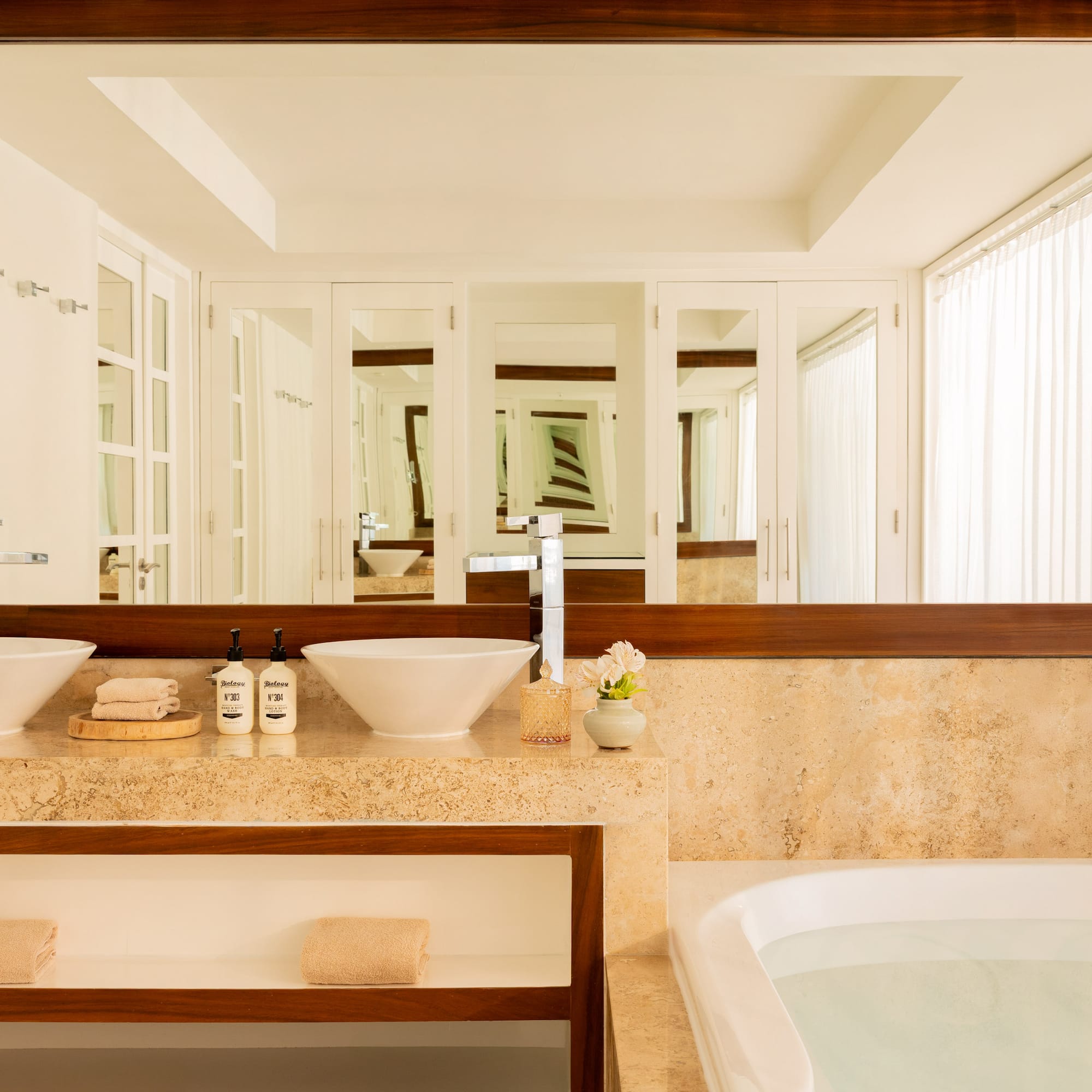 Modern bathroom with double vessel sinks, marble vanity, large mirror, and bathtub.