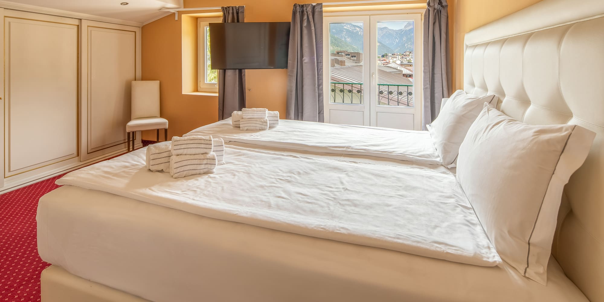 Hotel bedroom with twin beds, white bedding, and balcony mountain view.