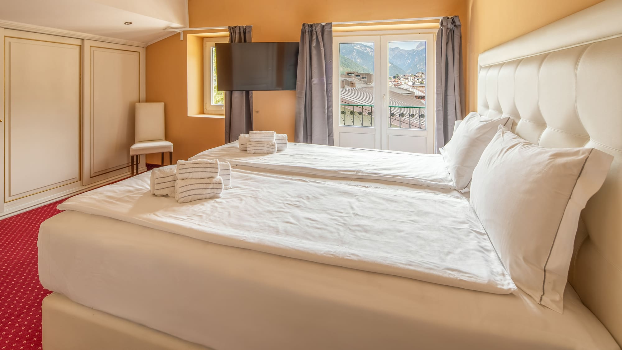 Hotel bedroom with twin beds, white bedding, and balcony mountain view.